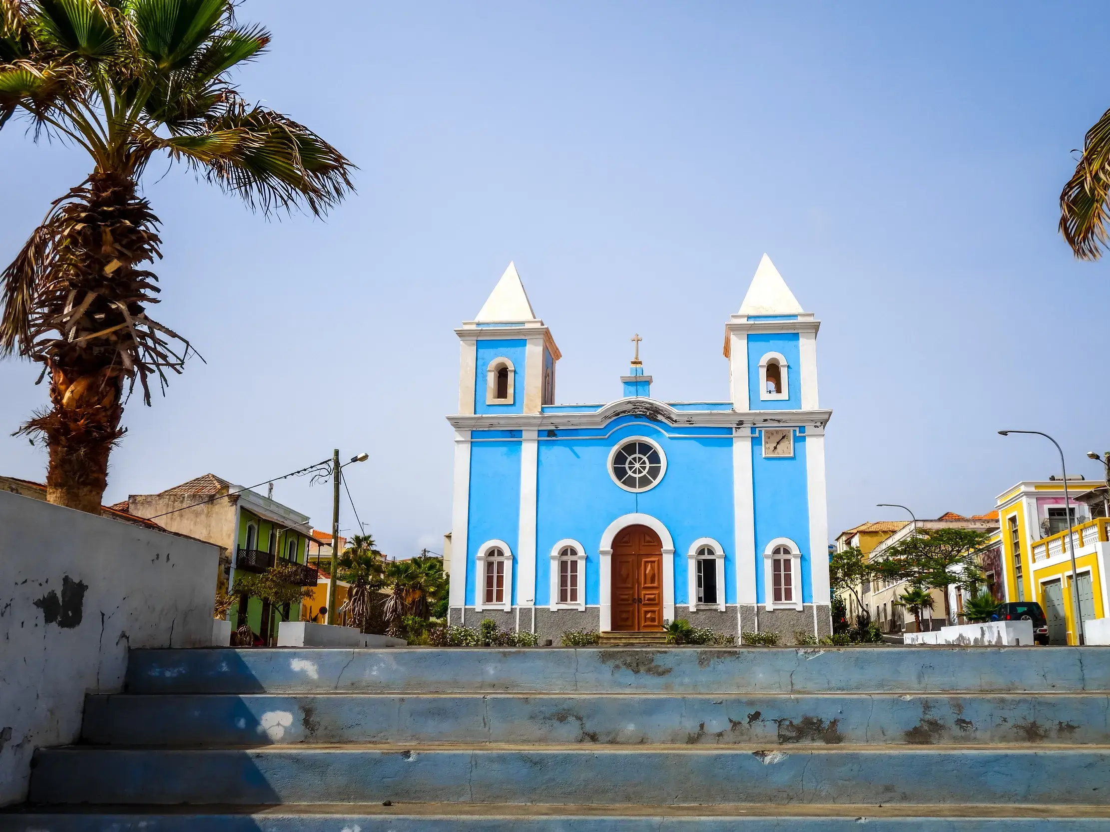 Blick über eine breite Steintreppe auf die leuchtend blaue Fassade der Kirche Igreja Nossa Senhora da Conceição in São Filipe, Fogo.