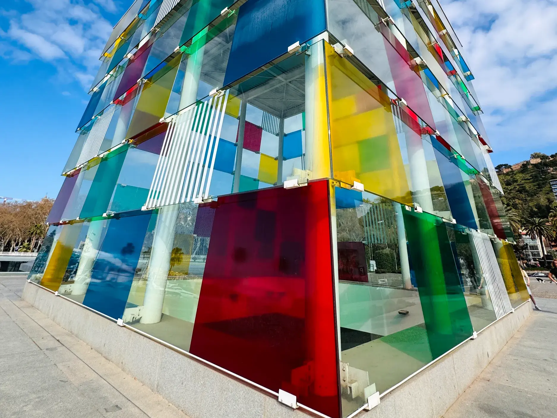 Der farbenfrohe Glaswürfel des Centre Pompidou an der Hafenpromenade von Málaga unter blauem Himmel in Andalusien.