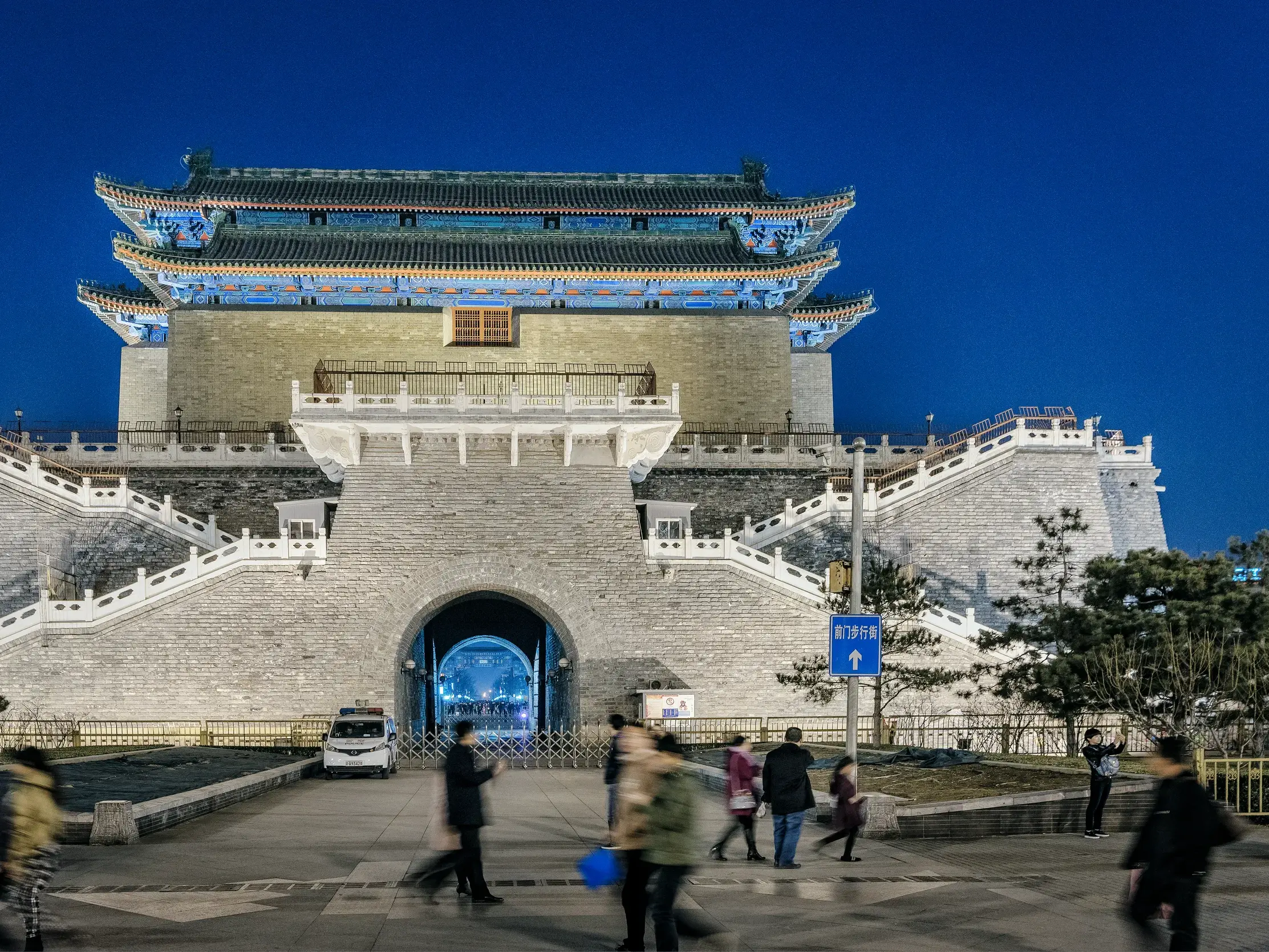 Das mächtige, historische Zhengyangmen-Tor in Beijing, nachts eindrucksvoll beleuchtet, während Menschen davor spazieren.