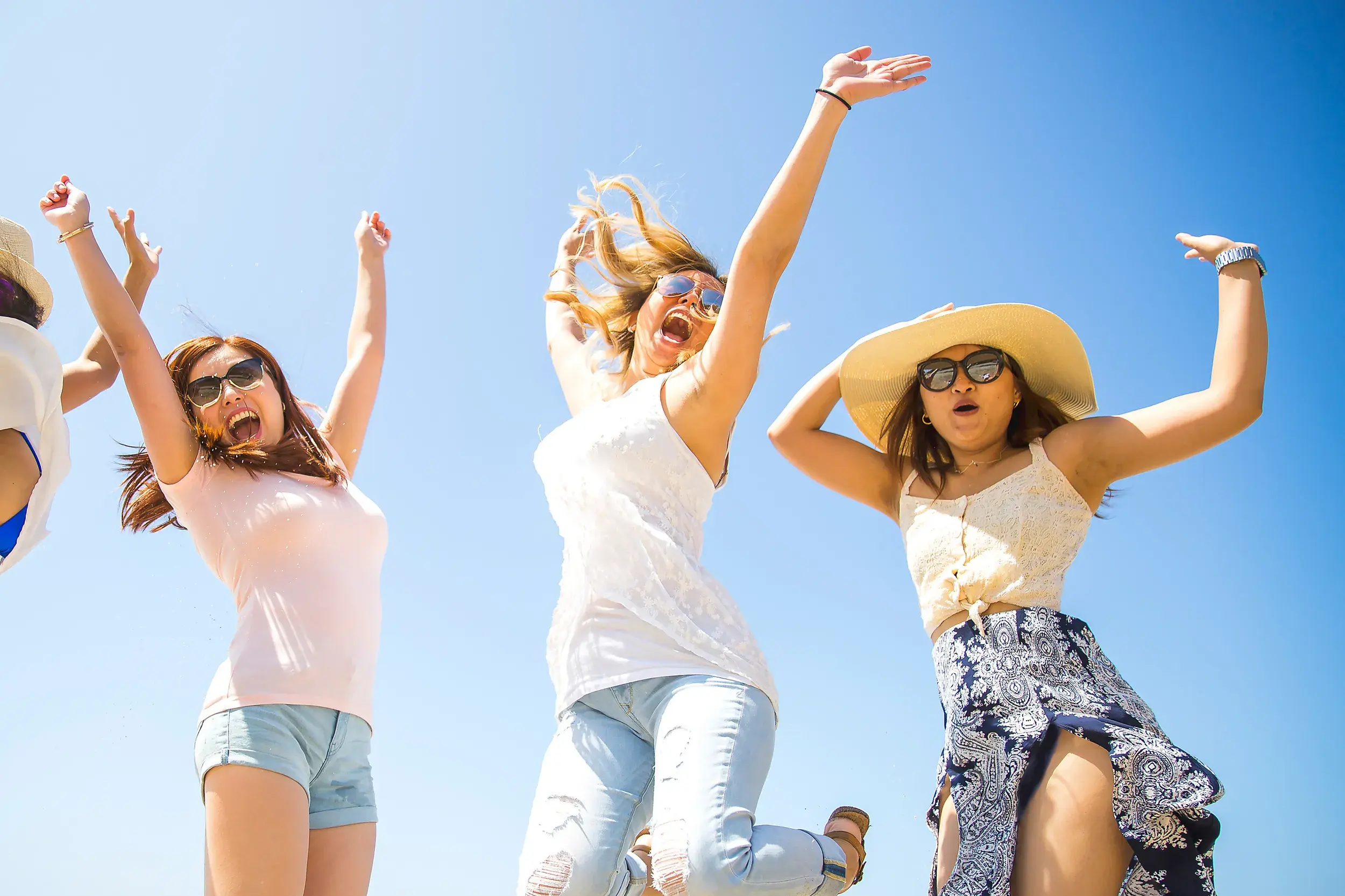 Vier junge Frauen springen auf einer Gruppenreise für junge Leute in Griechenland ausgelassen und lachend in die Luft.