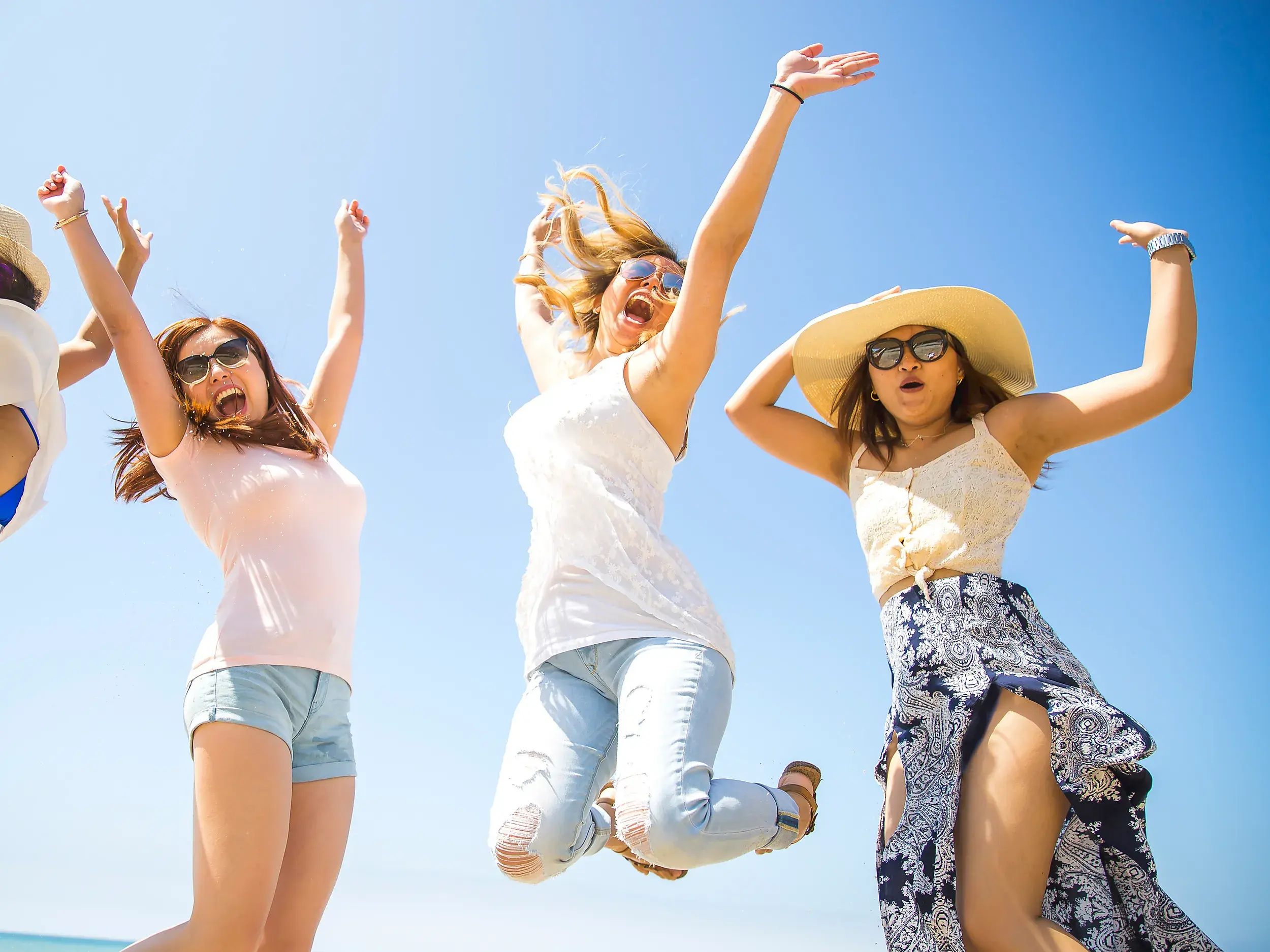Vier junge Frauen springen auf einer Gruppenreise für junge Leute in Griechenland ausgelassen und lachend in die Luft.