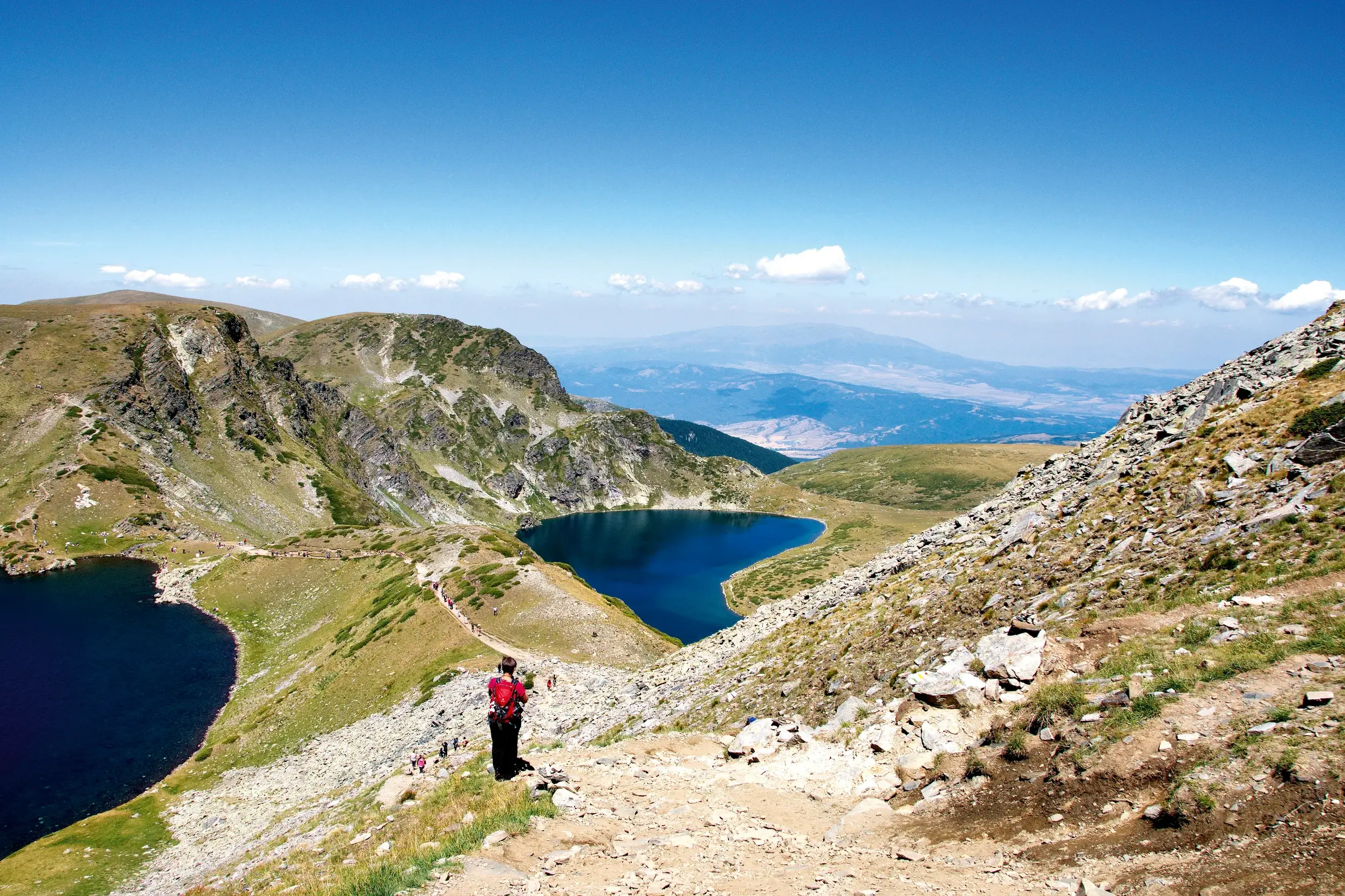 Ein Wanderer auf einem steinigen Pfad blickt auf die tiefblauen Bergseen der "Sieben Seen" im Rila-Gebirge in Bulgarien.