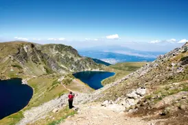 Ein Wanderer auf einem steinigen Pfad blickt auf die tiefblauen Bergseen der "Sieben Seen" im Rila-Gebirge in Bulgarien.