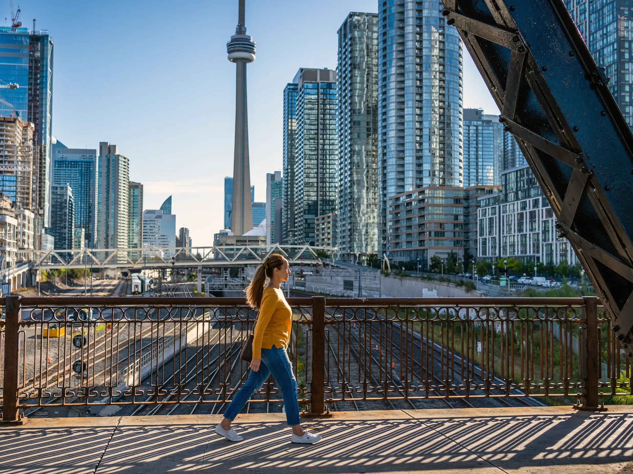 Eine Teilnehmerin einer Studienreise spaziert über eine Brücke mit Blick auf die Skyline von Toronto und den CN Tower.