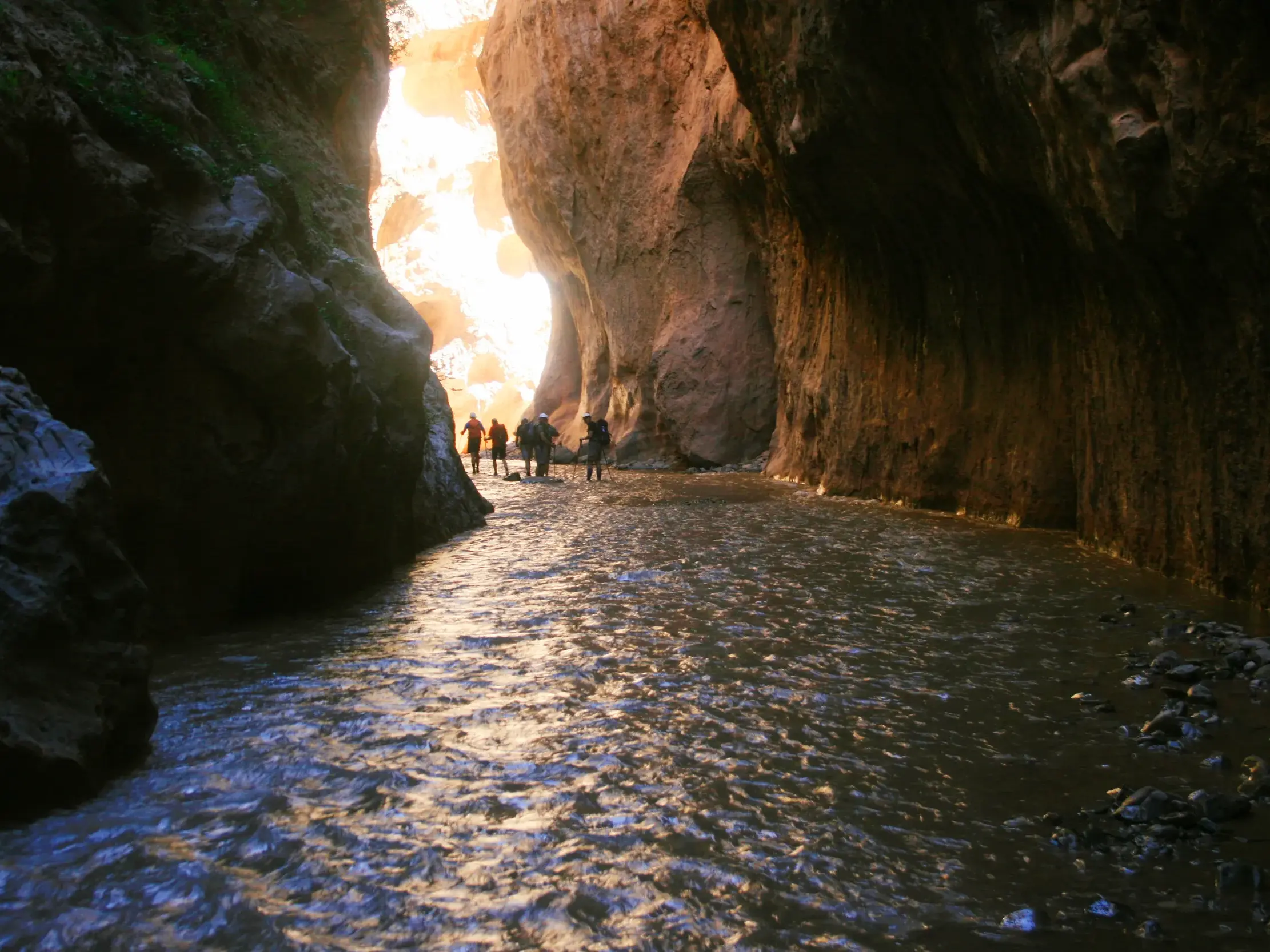 Eine Trekking-Gruppe durchwatet den Fluss in der beeindruckenden, von hohen Felswänden umgebenen Mgoun-Schlucht in Marokko.