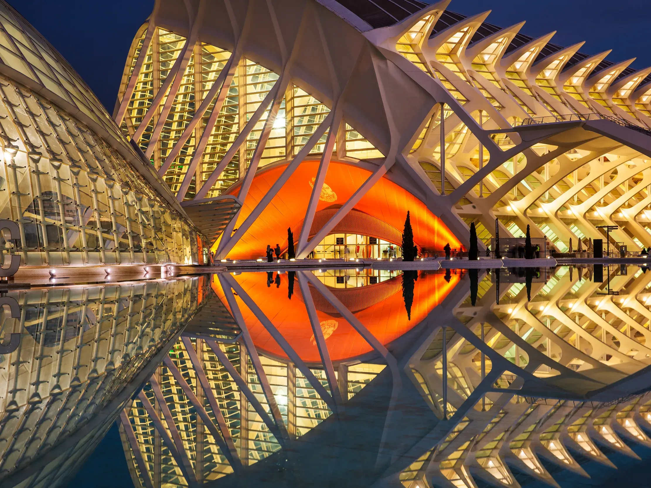Beleuchtete, futuristische Architektur der Stadt der Künste und Wissenschaften in Valencia bei Nacht, die sich im Wasser spiegelt.