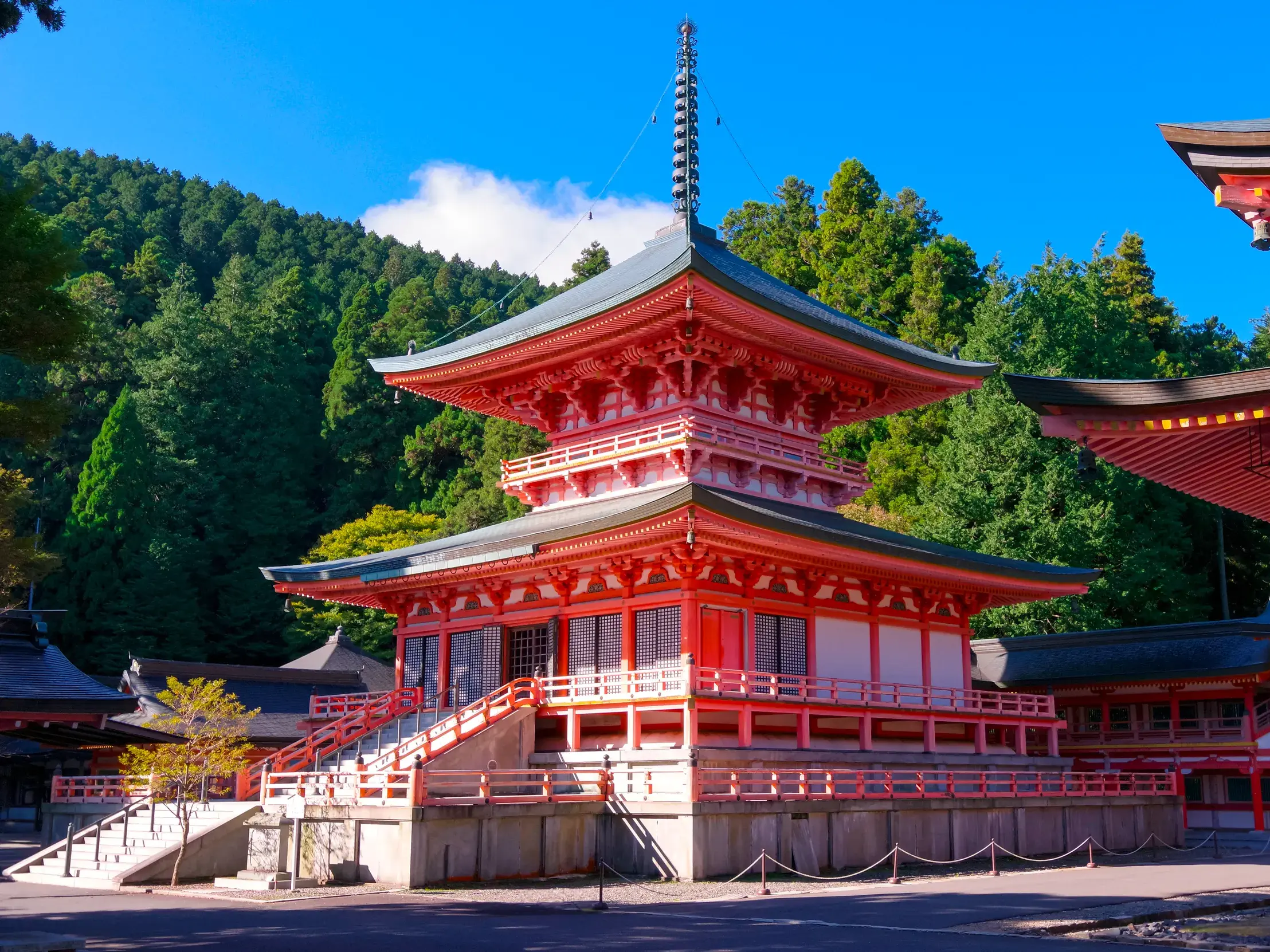 Leuchtend rote Pagode des Enryaku-ji Tempels auf dem Klosterberg Hieisan, umgeben von dichten, grünen Wäldern bei Sonnenschein.