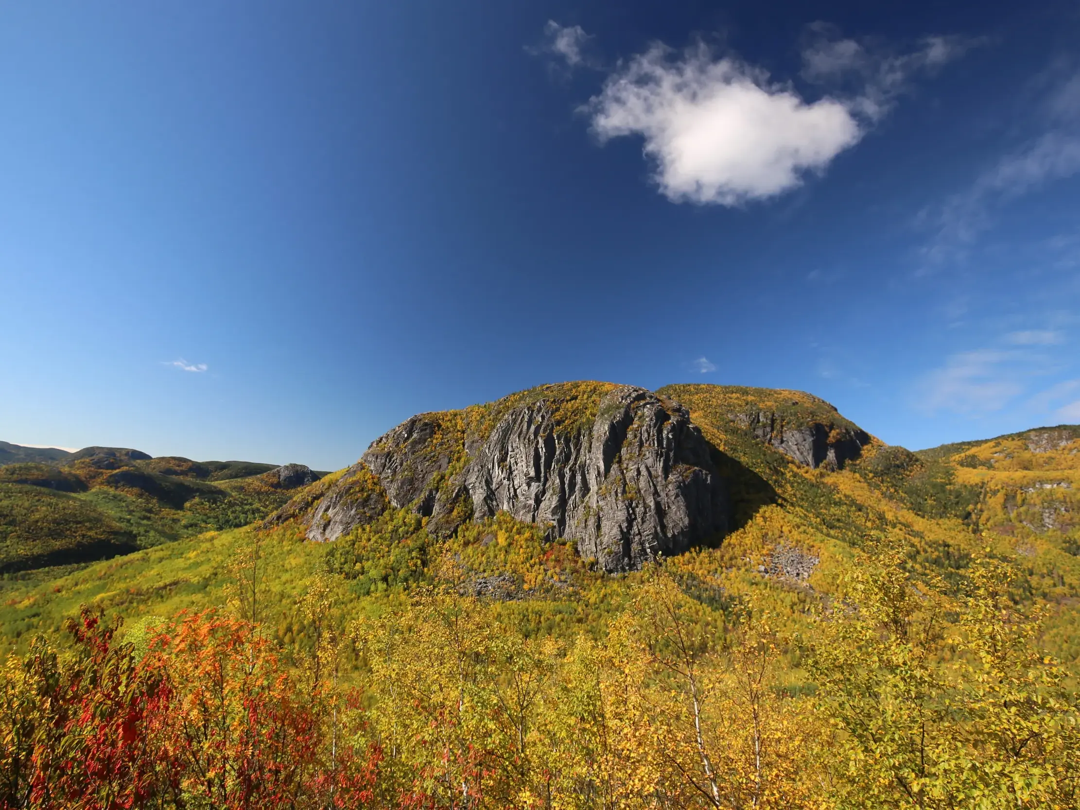 Eine felsige Bergkuppe erhebt sich aus den farbenprächtigen Wäldern des Indian Summer im Grands-Jardins-Nationalpark.