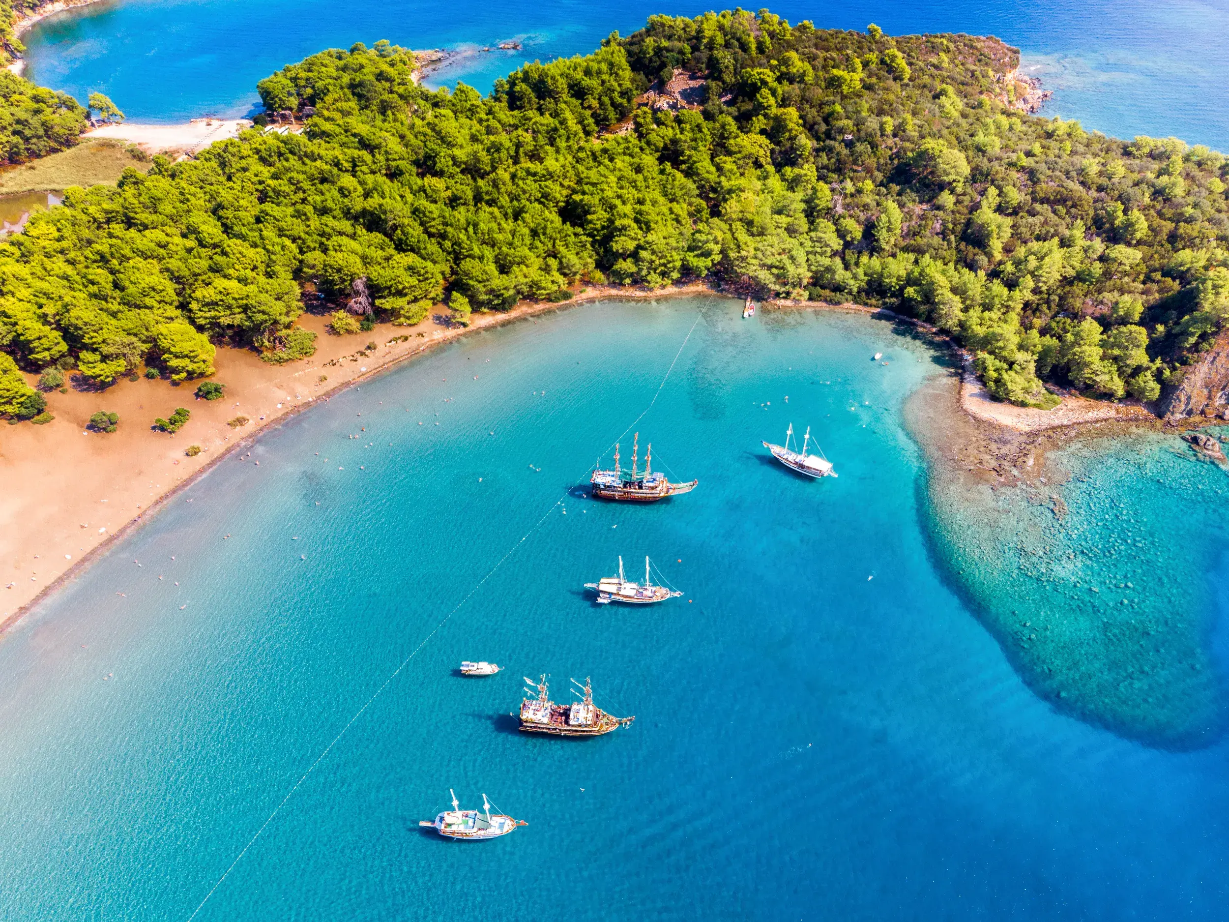 Malerische Bucht der antiken Stadt Phaselis aus der Luft, mit ankernden Ausflugsbooten im türkisfarbenen Mittelmeer.