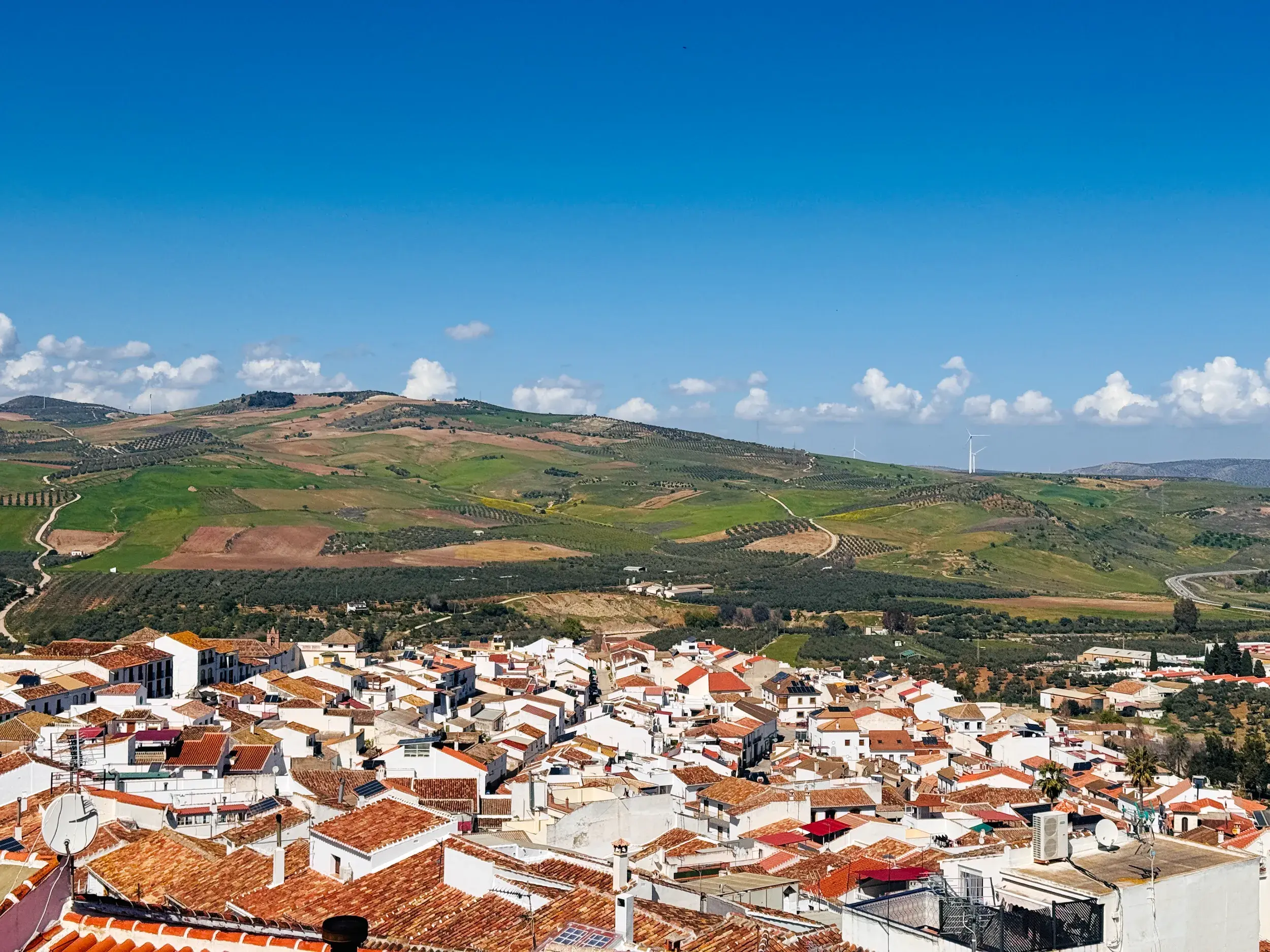 Panoramablick über die terrakottafarbenen Dächer eines weißen Dorfes in die weite, hügelige Landschaft Andalusiens.