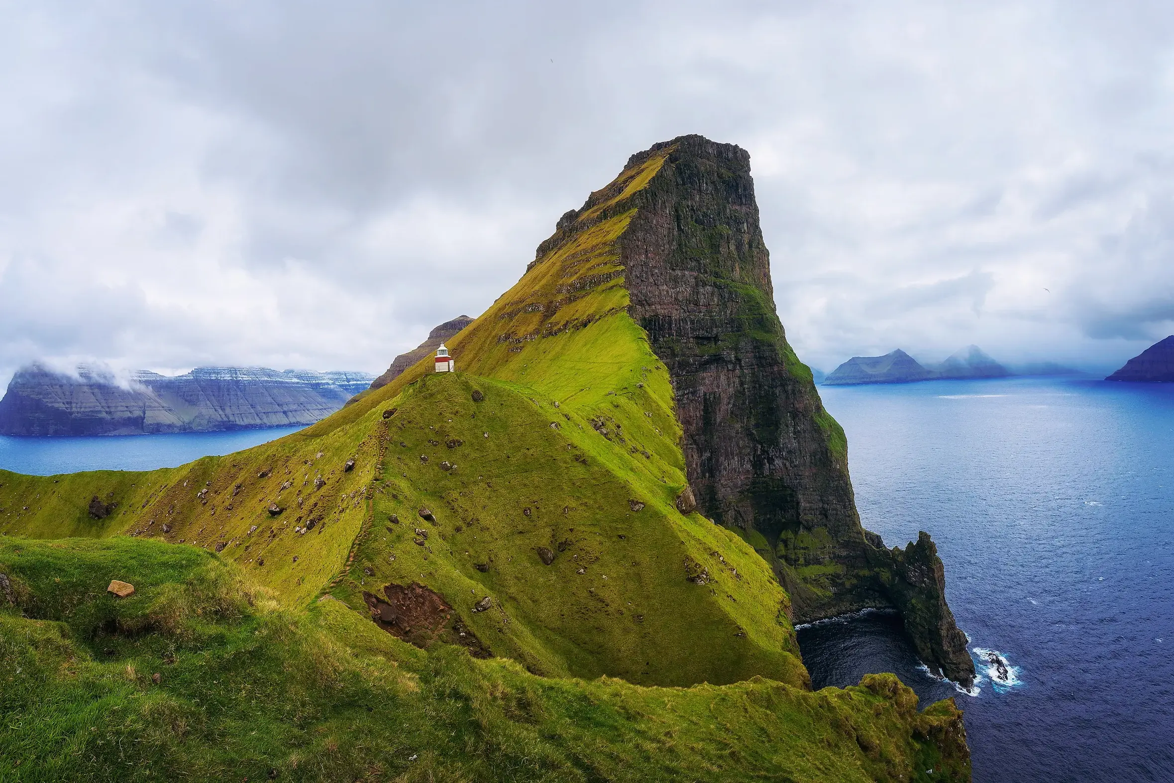 Der Leuchtturm Kallur auf Kalsoy thront auf einem schmalen, grünen Felsgrat hoch über dem Atlantik der Färöer-Inseln.