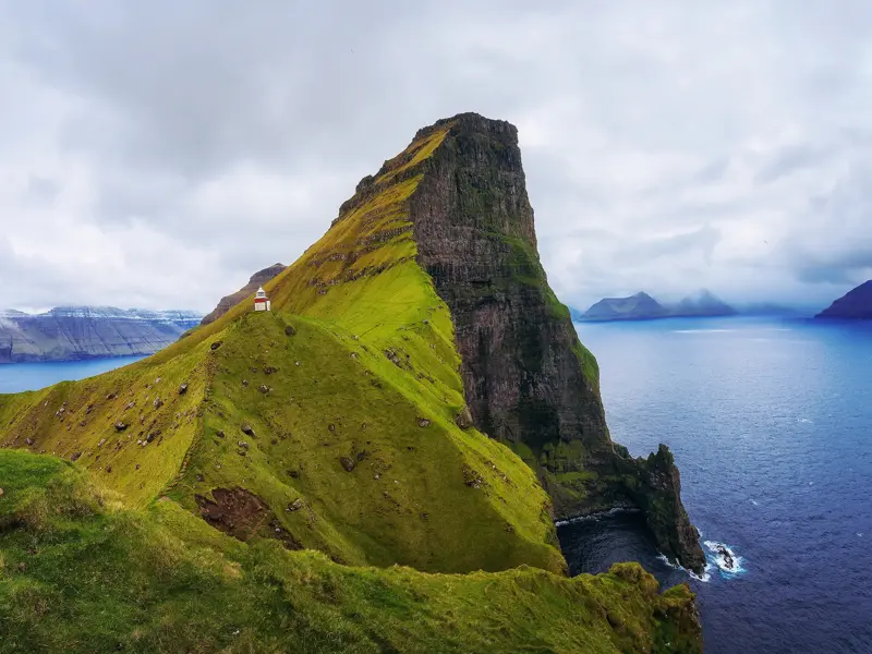 Der Leuchtturm Kallur auf Kalsoy thront auf einem schmalen, grünen Felsgrat hoch über dem Atlantik der Färöer-Inseln.