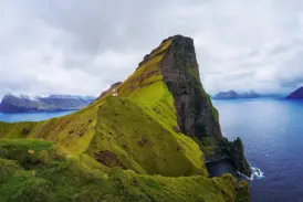 Der Leuchtturm Kallur auf Kalsoy thront auf einem schmalen, grünen Felsgrat hoch über dem Atlantik der Färöer-Inseln.