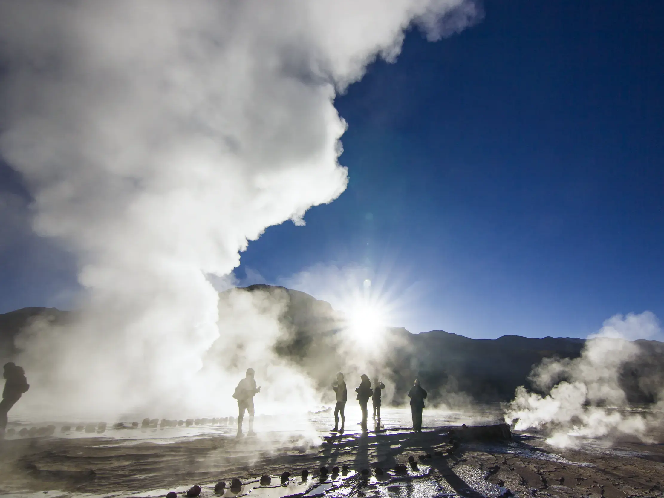 Junge Reisegruppe beobachtet die spektakulären Dampfsäulen der El Tatio Geysire bei Sonnenaufgang in der Atacamawüste Chiles.