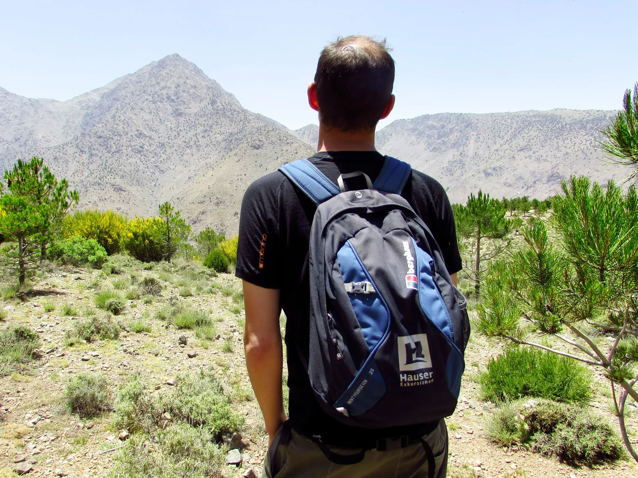 Ein Wanderer mit Hauser Exkursionen Rucksack blickt beim Trekking in Marokko auf die sonnigen Gipfel des Hohen Atlas.