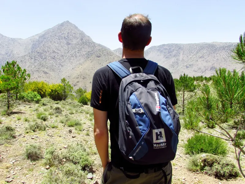 Ein Wanderer mit Hauser Exkursionen Rucksack blickt beim Trekking in Marokko auf die sonnigen Gipfel des Hohen Atlas.