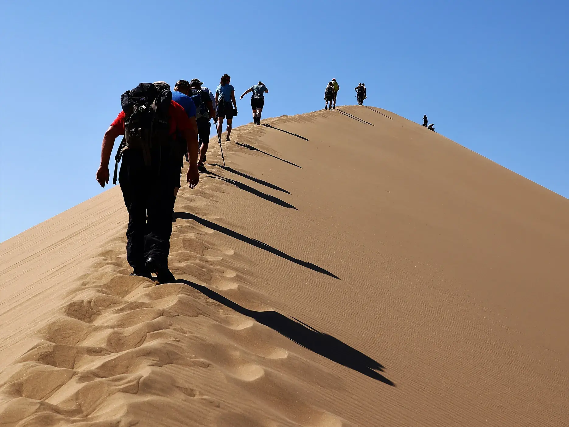 Eine Trekking-Gruppe mit Rucksäcken wandert auf dem Grat der Singenden Düne im Altyn-Emel-Nationalpark in Kasachstan.