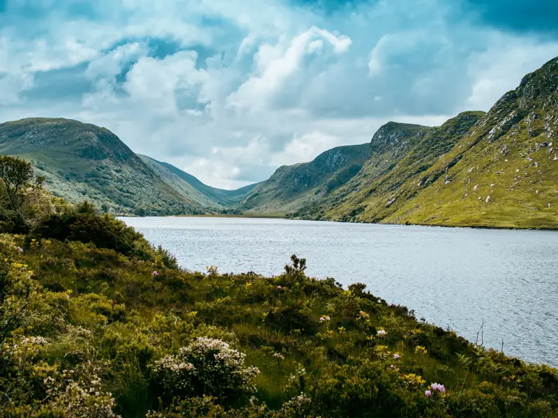 Malerischer Blick über den Lough Beagh im Glenveagh Nationalpark, eingerahmt von üppig grünen Bergen unter wolkigem Himmel.