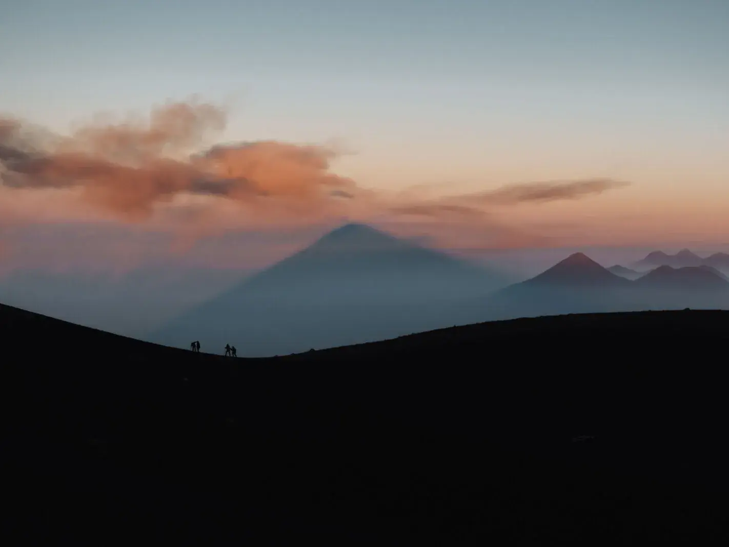 Eine kleine Gruppe Wanderer beobachtet beim Sonnenaufgang den Schatten des Vulkans Acatenango in Guatemala.