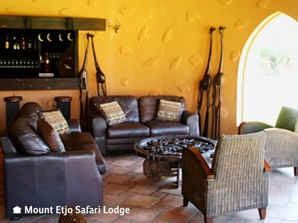 Rustikaler Loungebereich in der Mount Etjo Safari Lodge in Namibia mit Ledersofas und afrikanischer Dekoration.
