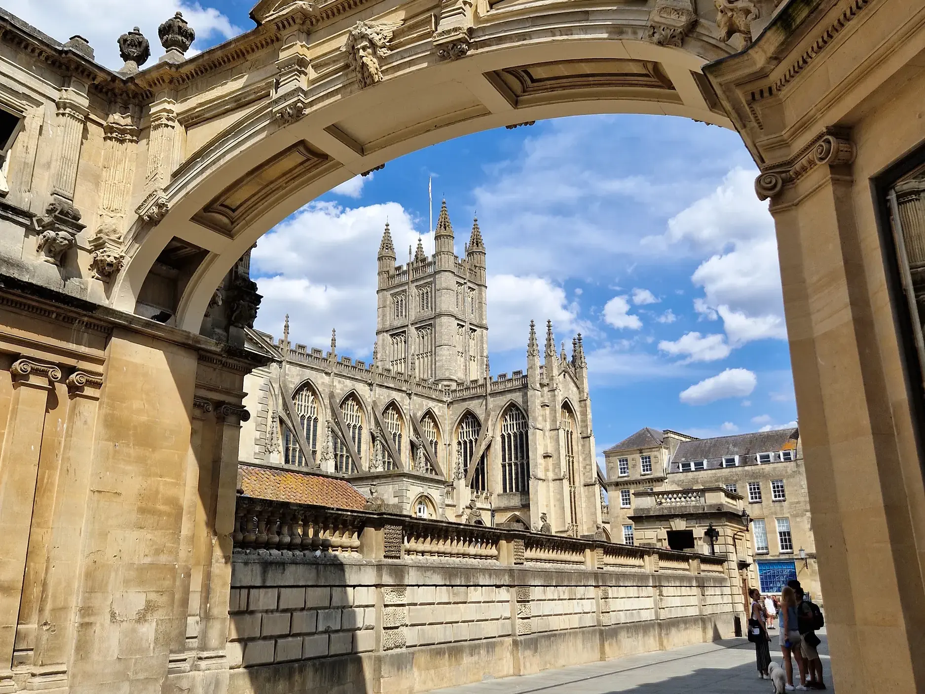 Imposante gotische Kirche in der Bäderstadt Bath, kunstvoll gerahmt von einem steinernen Torbogen unter blauem Himmel.