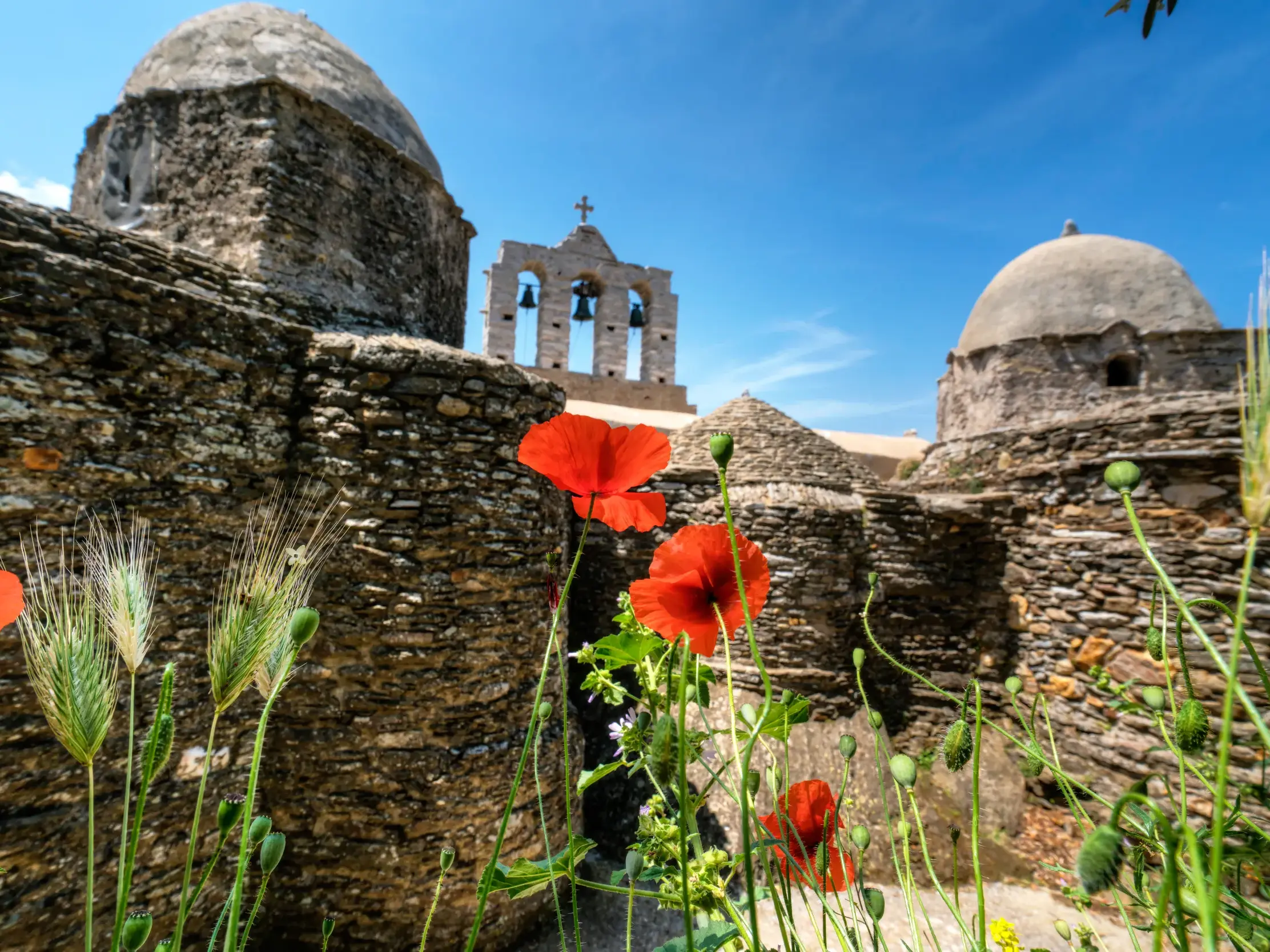 Nahe dem Heiligtum der Demeter auf Naxos blühen rote Mohnblumen vor einer alten Steinkirche mit Glockenturm.