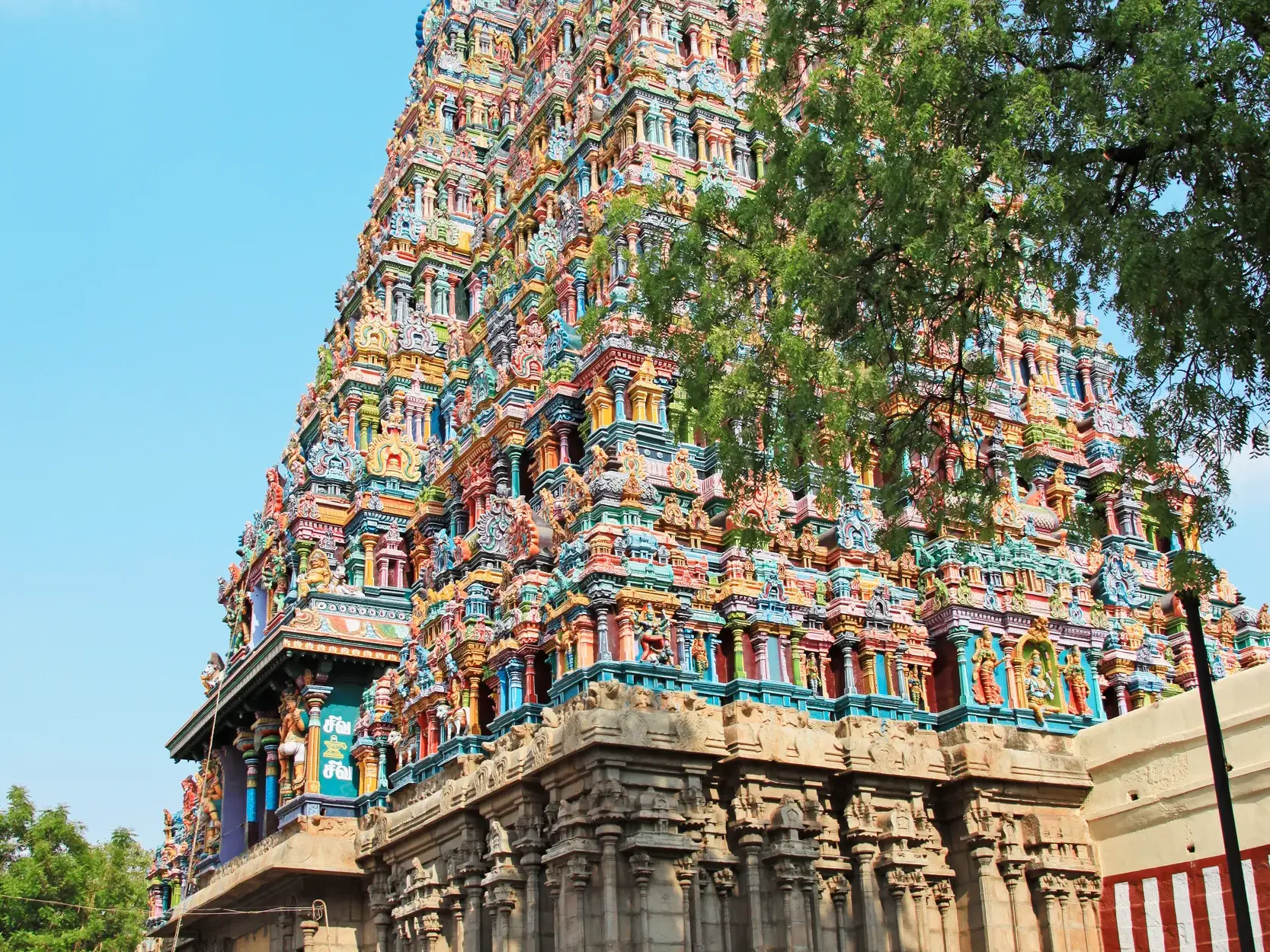 Der farbenprächtige Turm des Minakshi-Tempels in Madurai mit unzähligen Götterfiguren unter blauem Himmel in Südindien.