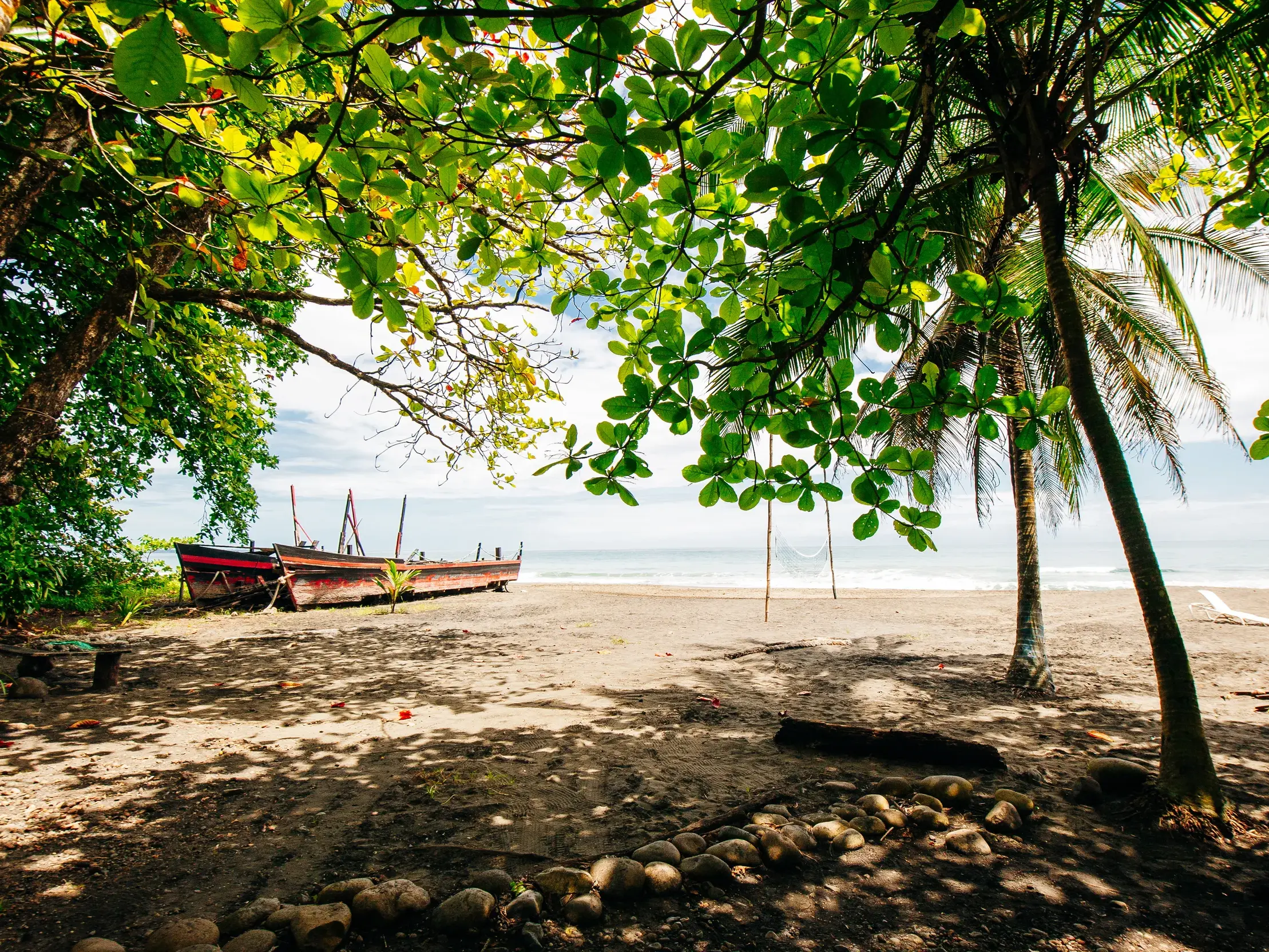 Holzboot am Sandstrand der Karibikküste Costa Ricas bei Puerto Viejo, umgeben von Palmen und tropischem Regenwald.
