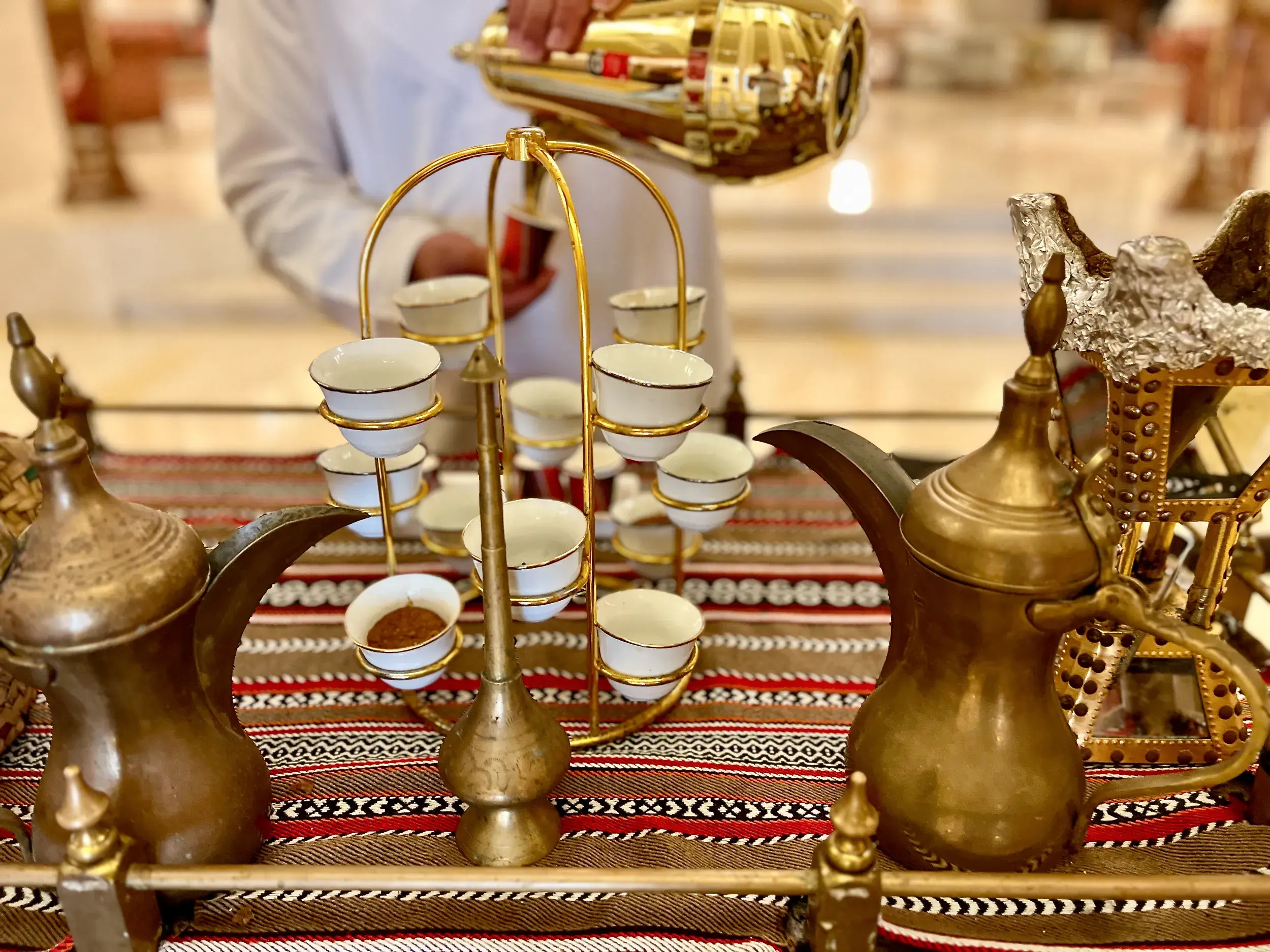 Omanische Gastfreundschaft: Ein Mann serviert traditionellen Kaffee aus einer goldenen Dallah in kleine weiße Tassen.