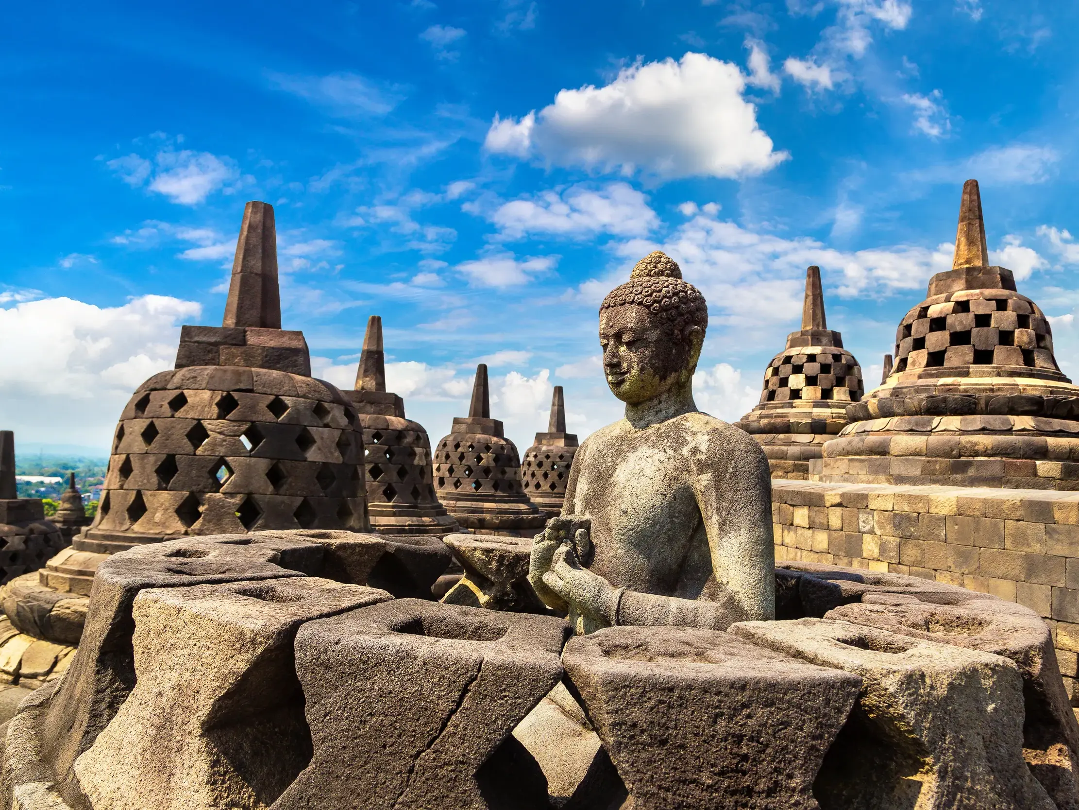 Steinerne Buddha-Statue und glockenförmige Stupas auf der weltgrößten buddhistischen Tempelanlage Borobudur auf Java.
