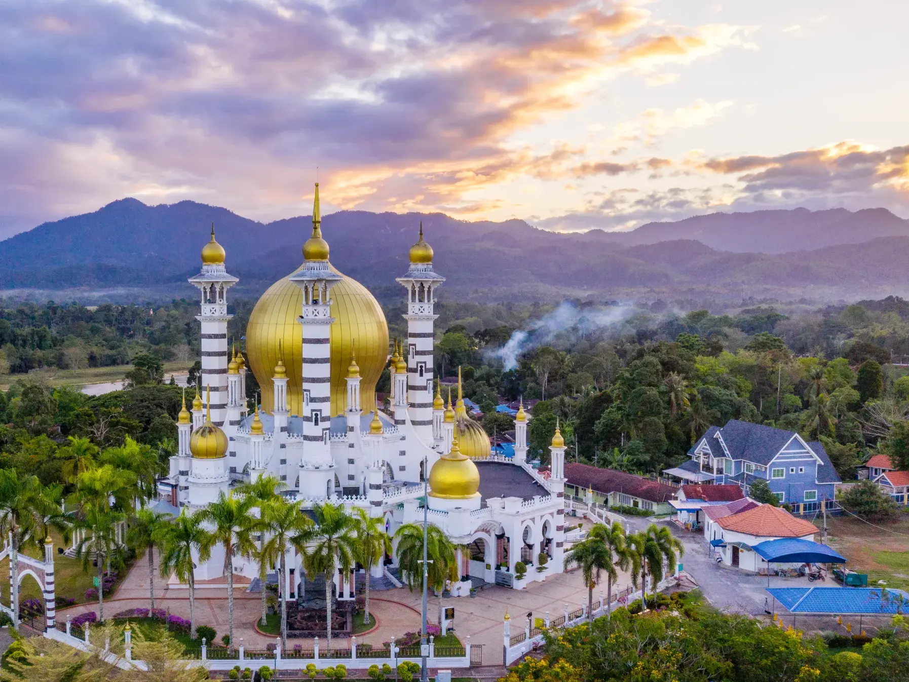Die prächtige Ubudiah-Moschee in Malaysia mit ihren goldenen Kuppeln und Minaretten vor einer malerischen Bergkulisse bei Dämmerung.