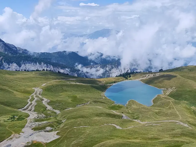Türkisblauer Gletschersee inmitten grüner Almwiesen im Korab-Koritnik Naturpark in Albanien mit Bergpanorama im Hintergrund.