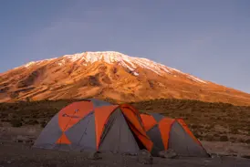 Trekking-Zelte im Camp am Northern Circuit vor dem schneebedeckten Gipfel des Kilimanjaro im Morgenlicht.
