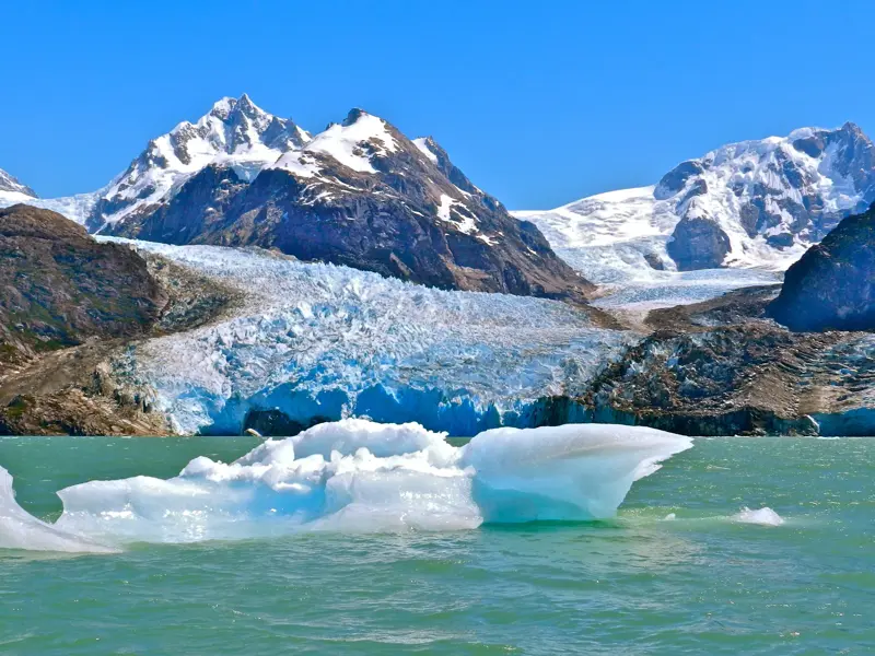 Ein Eisberg treibt auf dem türkisen Lago Leones vor dem massiven Leones Gletscher und den schneebedeckten Gipfeln Patagoniens.