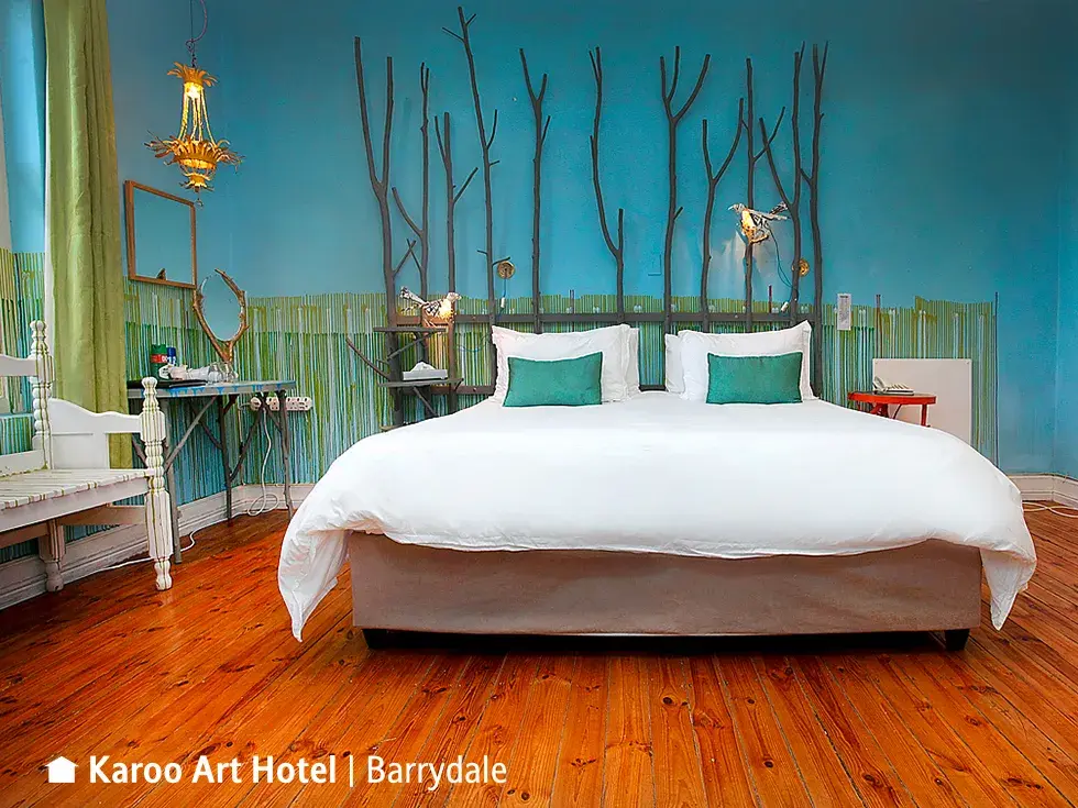 Künstlerisch gestaltetes Hotelzimmer im Karoo Art Hotel mit Doppelbett vor einer türkisen Wand mit Ast-Skulptur als Kopfteil.