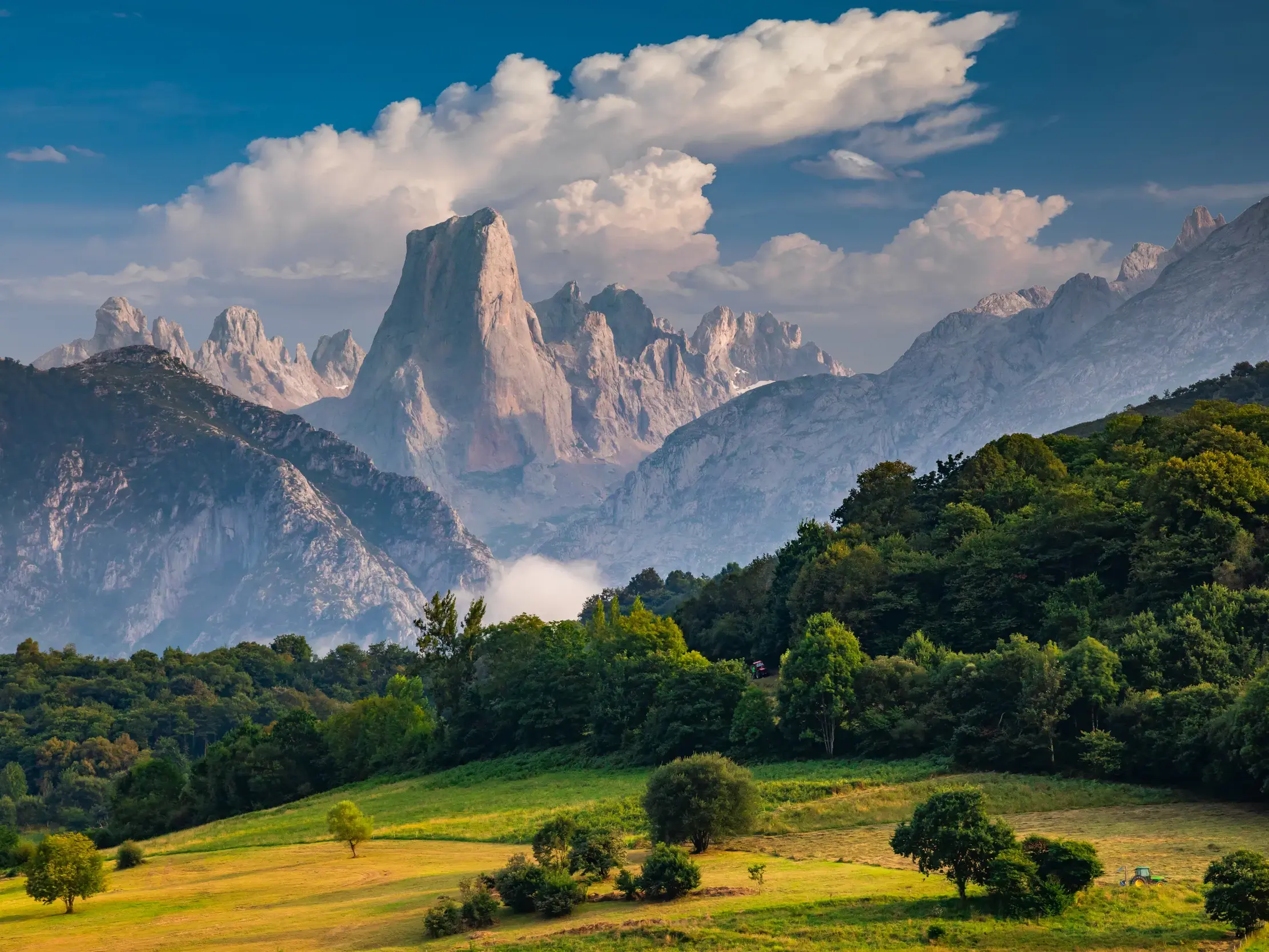 Grüne Hügel und Wälder vor dem markanten Felsgipfel Naranjo de Bulnes im Nationalpark Picos de Europa in Asturien.