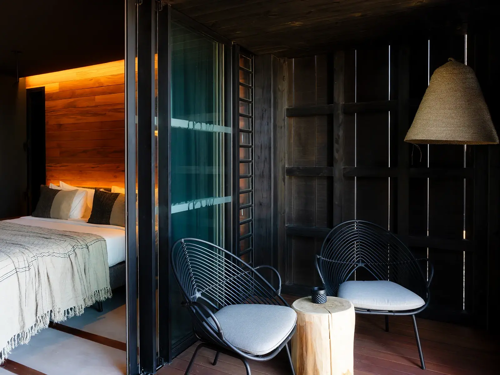 Modernes Hotelzimmer im Wood Hotel & Spa auf La Réunion mit dunklem Holzdesign, warmem Licht und möbliertem Balkon.
