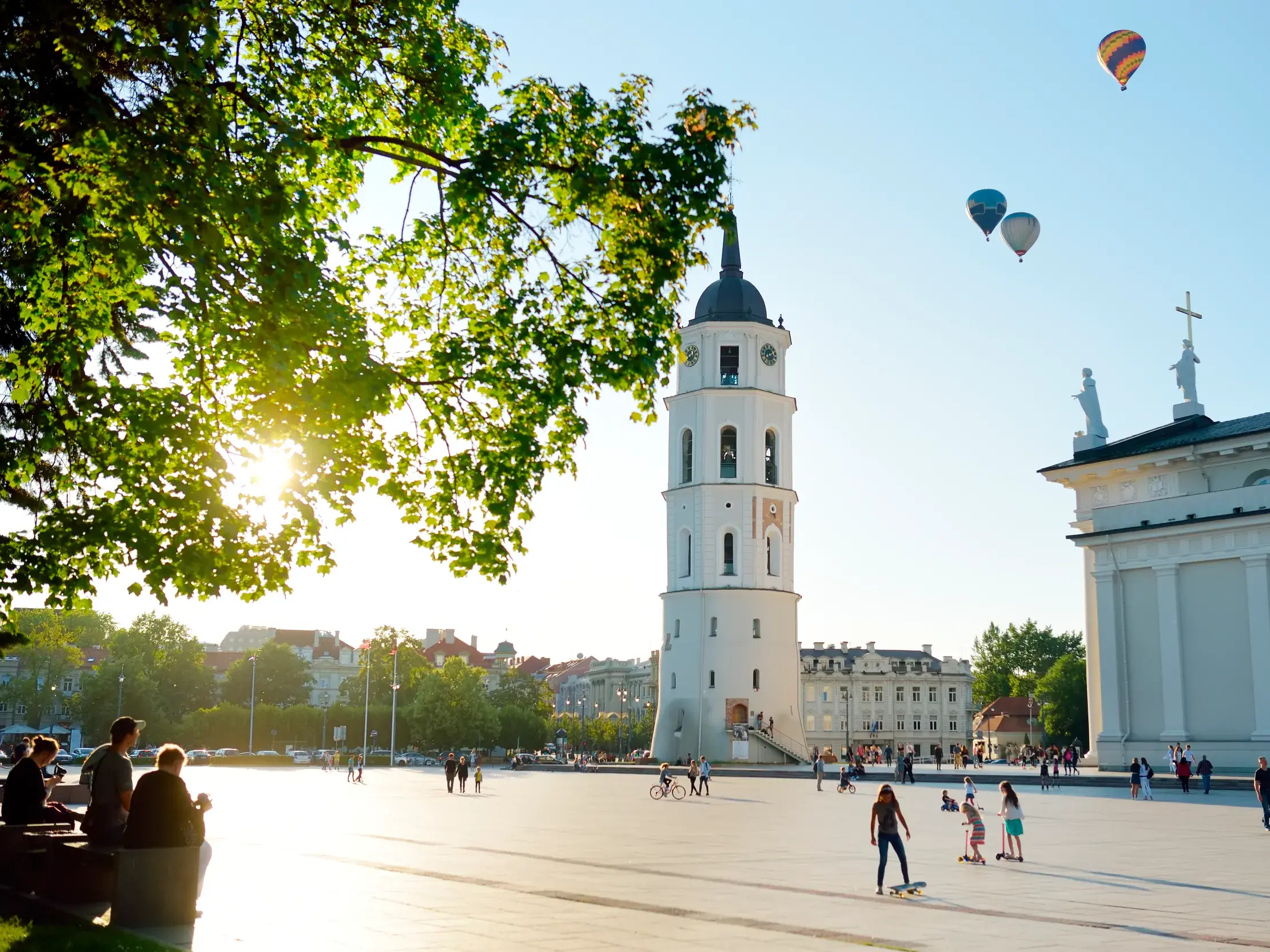 Sonniger Nachmittag auf dem Kathedralenplatz in Vilnius mit Glockenturm, Kathedrale und bunten Heißluftballons am Himmel.