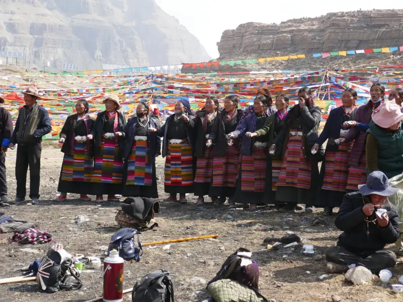 Tibetische Pilger in traditioneller Kleidung feiern gemeinsam während der Kora am heiligen Berg Kailash vor Gebetsfahnen.