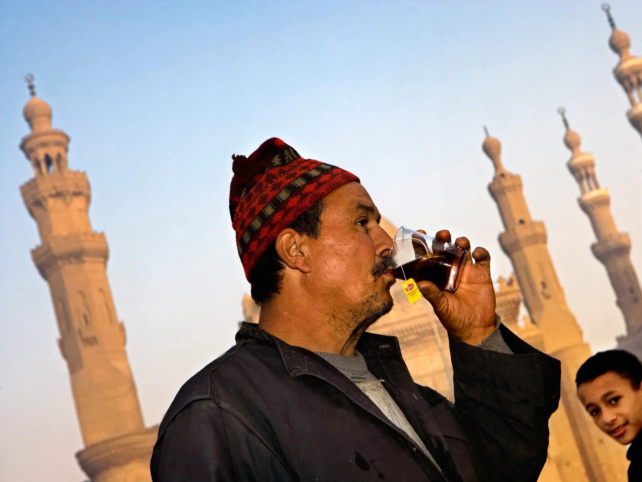 Einheimischer Mann mit Mütze genießt ein Glas Tee vor der Kulisse der Minarette der Al-Azhar-Moschee in Kairo.