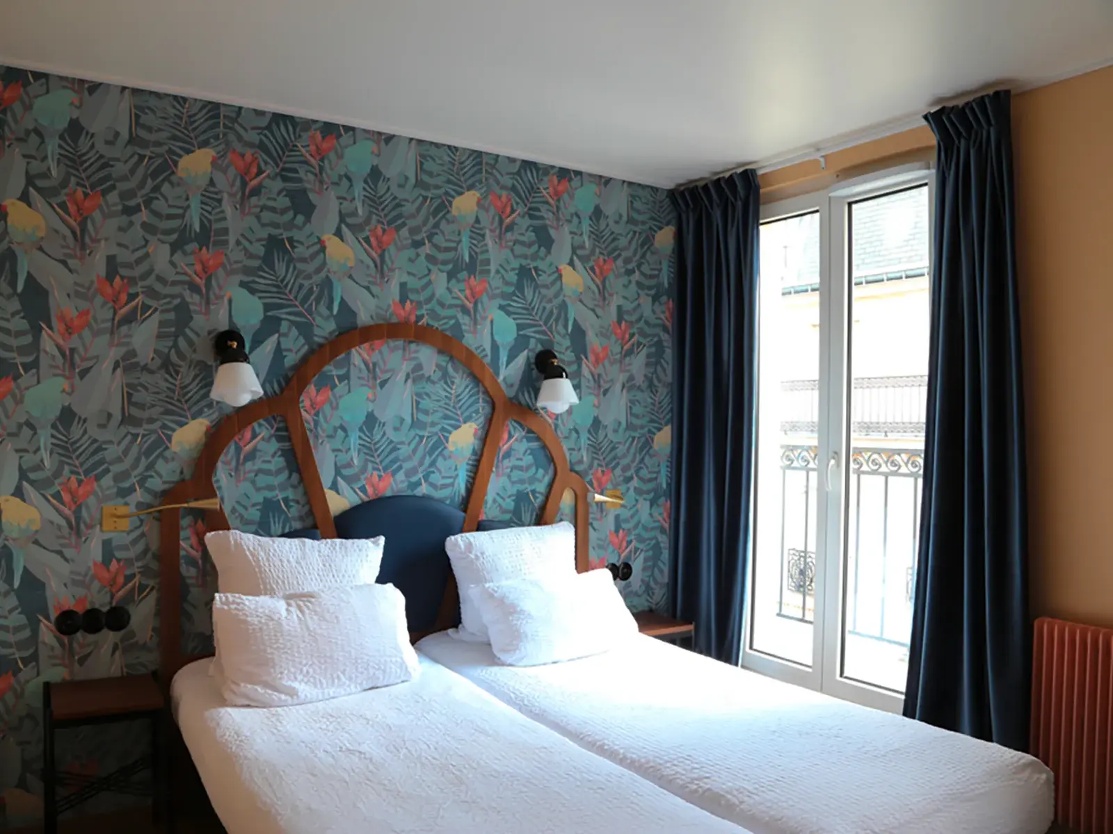 Einladendes Doppelzimmer im Hotel André Latin in Paris mit zwei Betten und einer Wand mit tropischer Blättertapete.