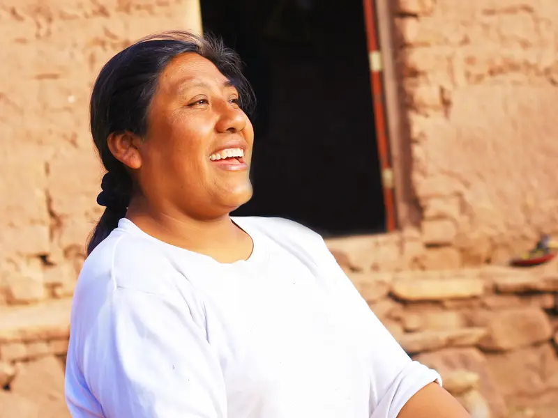 Eine einheimische Frau in der Atacama-Wüste lacht herzlich im Sonnenlicht vor einem traditionellen Lehmhaus in Chile.