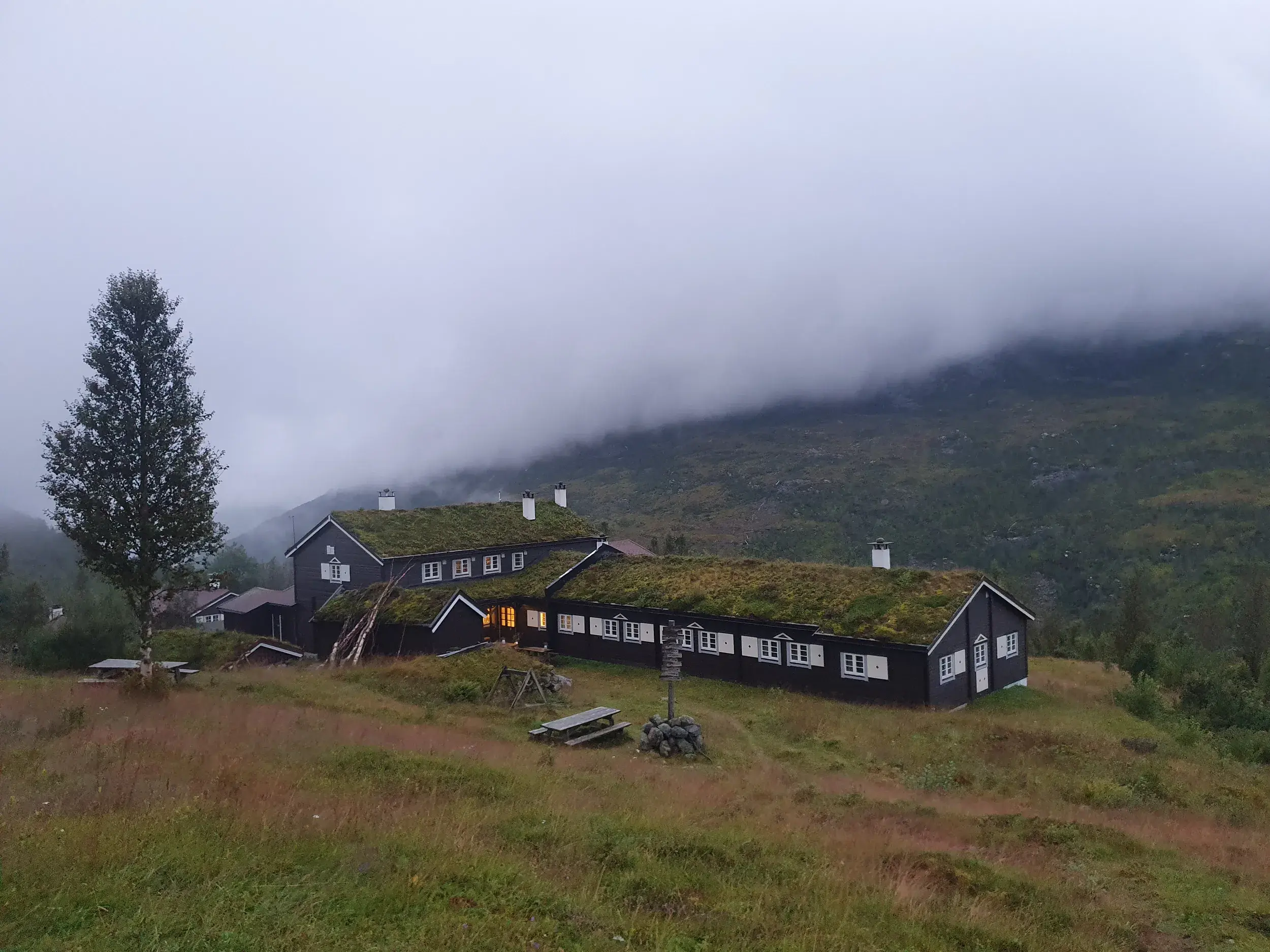Idyllische Berghütte Skogadalsbø mit typischem Grasdach auf einer Trekkingreise im nebligen Jotunheimen Nationalpark.