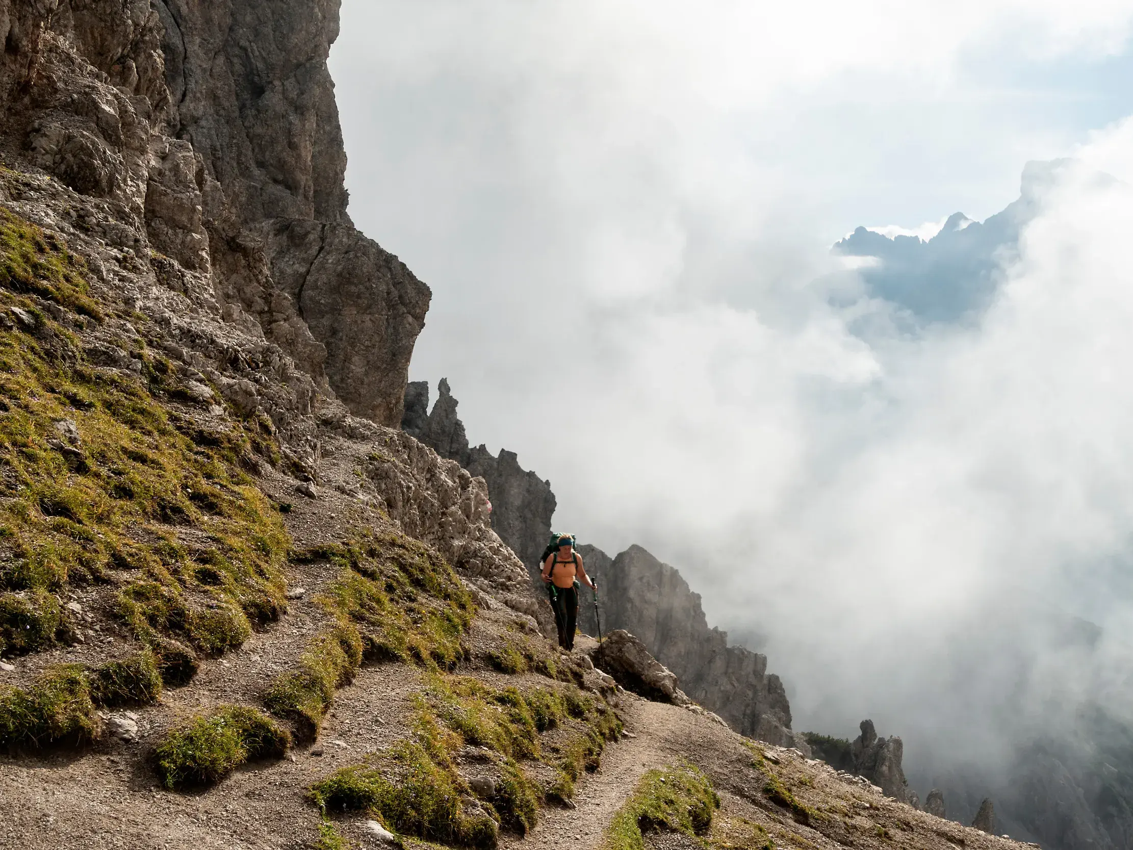 Wanderer mit Rucksack und Stöcken auf schmalem Pfad entlang der Erlspitzgruppe im wolkenverhangenen Karwendelgebirge.
