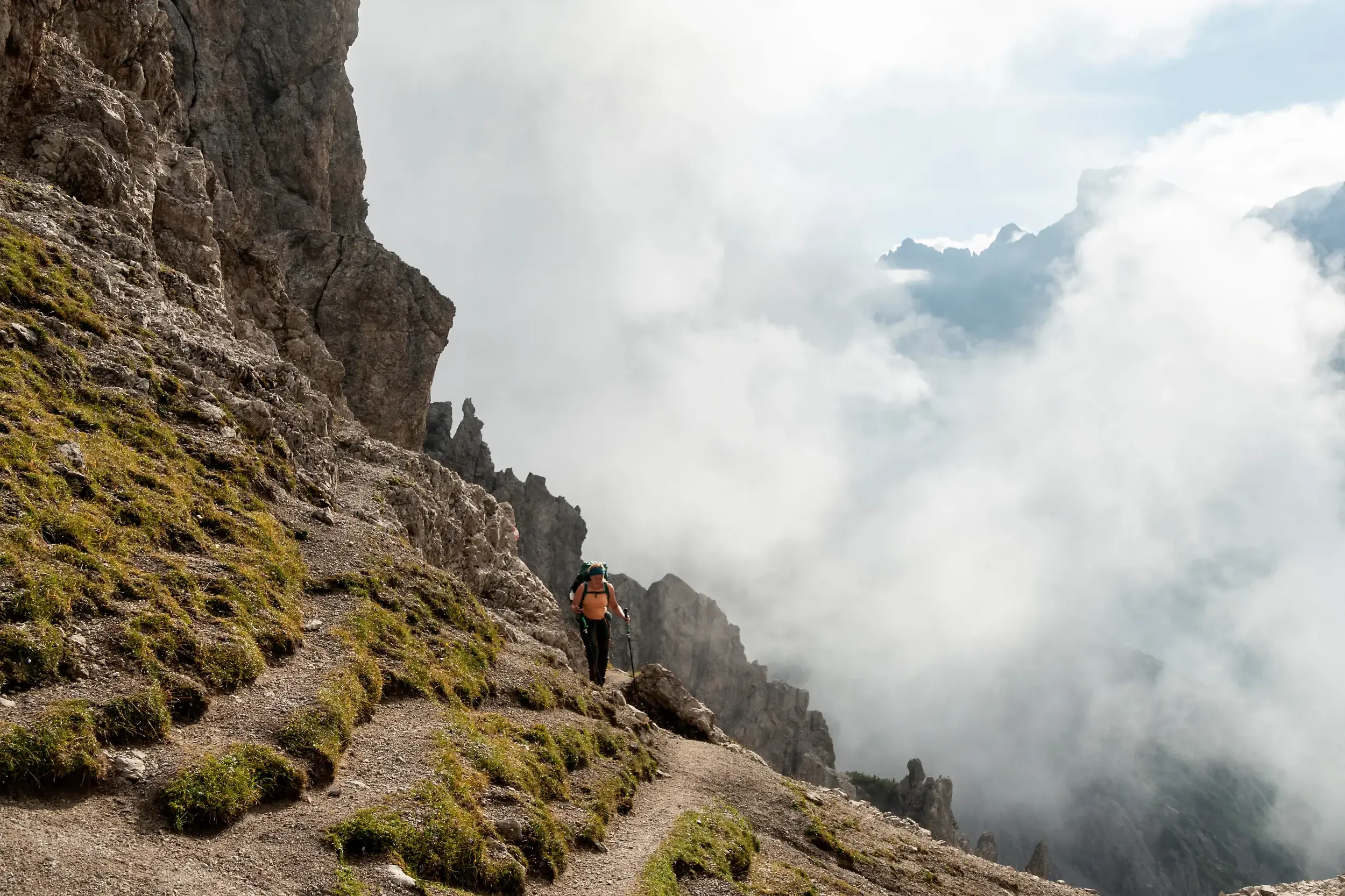 Wanderer mit Rucksack auf steilem Bergpfad beim Trekking im wilden Karwendelgebirge über einem dichten Wolkenmeer.