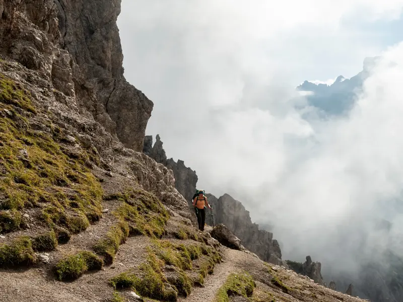 Wanderer mit Rucksack auf steilem Bergpfad beim Trekking im wilden Karwendelgebirge über einem dichten Wolkenmeer.
