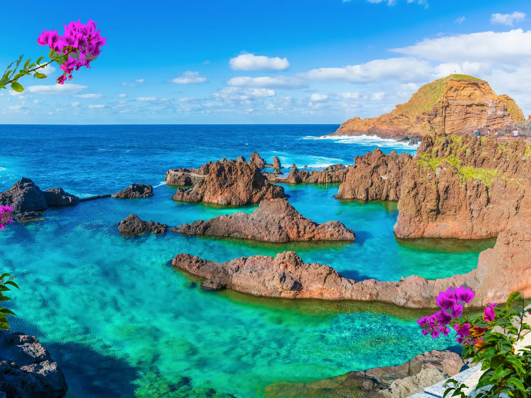 Sonnige Küstenlandschaft in Porto Moniz mit natürlichen Felsenpools, umgeben von dunklem Vulkangestein und dem blauen Atlantik.
