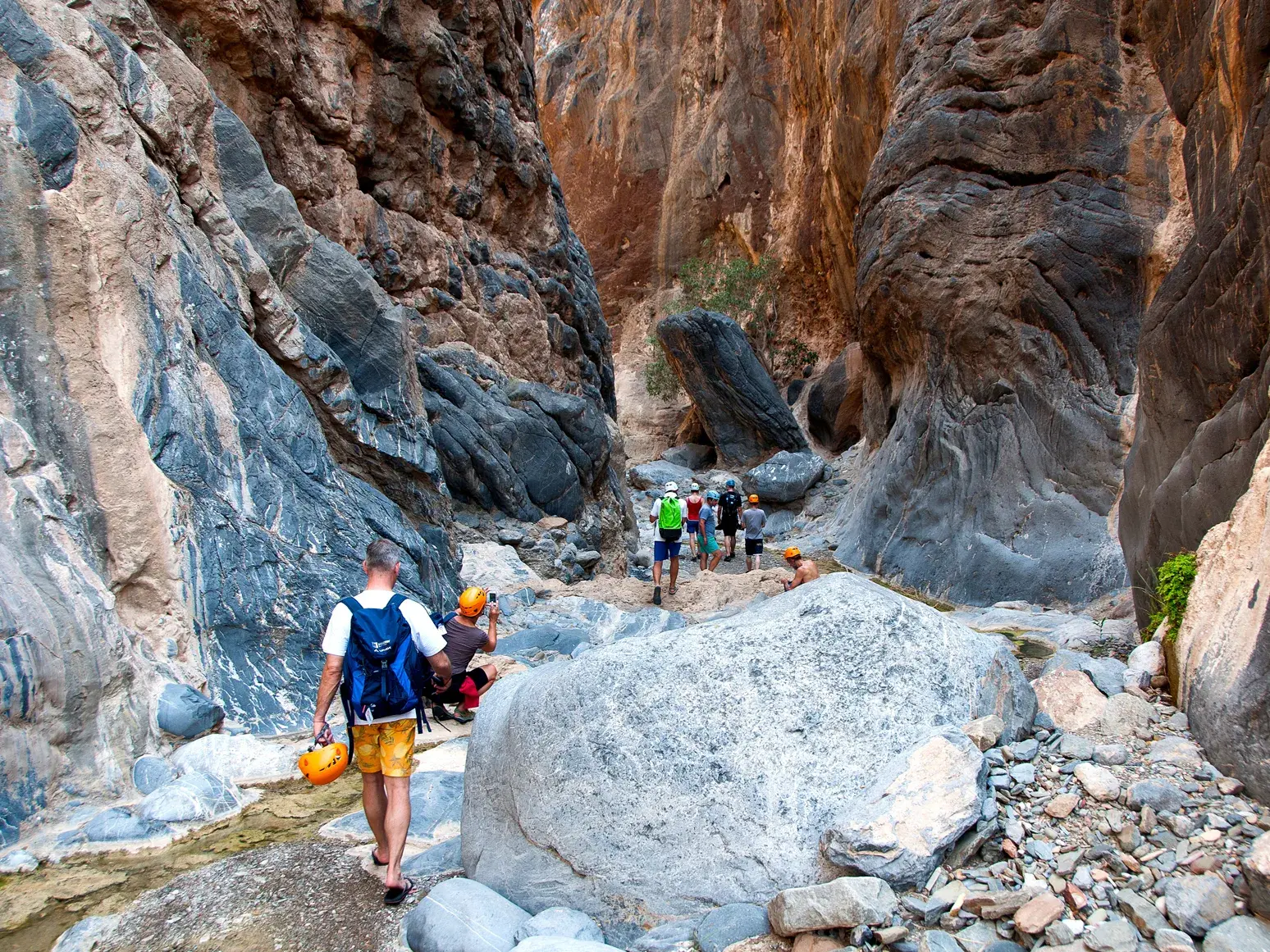Eine Hauser-Reisegruppe beim Trekking auf einem schmalen Pfad durch die enge, felsige Schlucht des Wadi Shab im Oman.