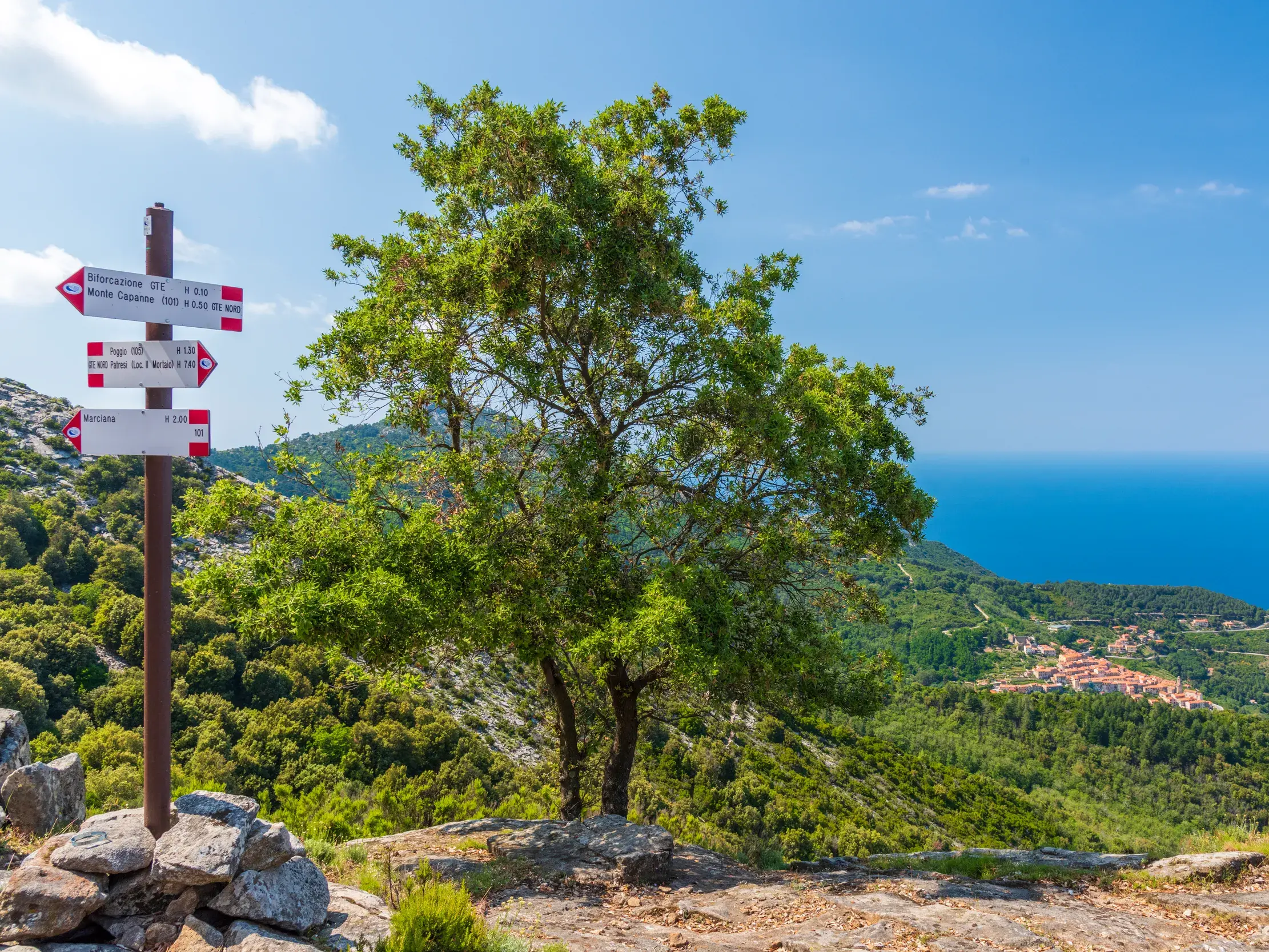 Wegweiser auf dem GTE-Trekkingweg auf Elba mit Panoramablick über die grüne Küstenlandschaft und das Mittelmeer.