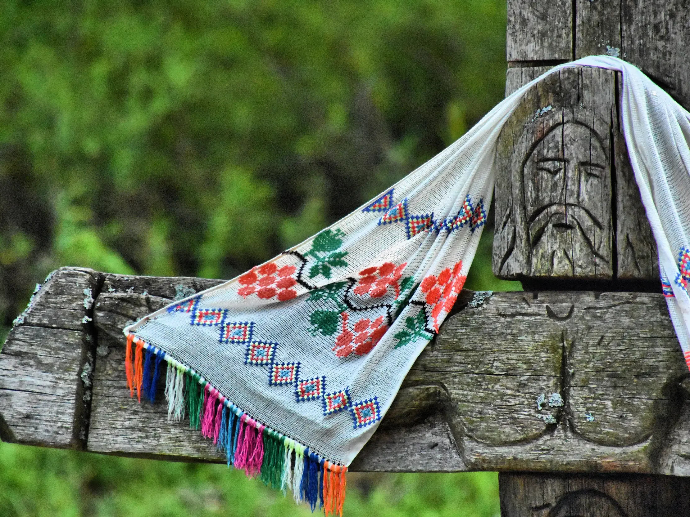 Besticktes Tuch mit bunten Fransen hängt über einer traditionellen Holzschnitzerei mit Gesicht in der Region Siebenbürgen.